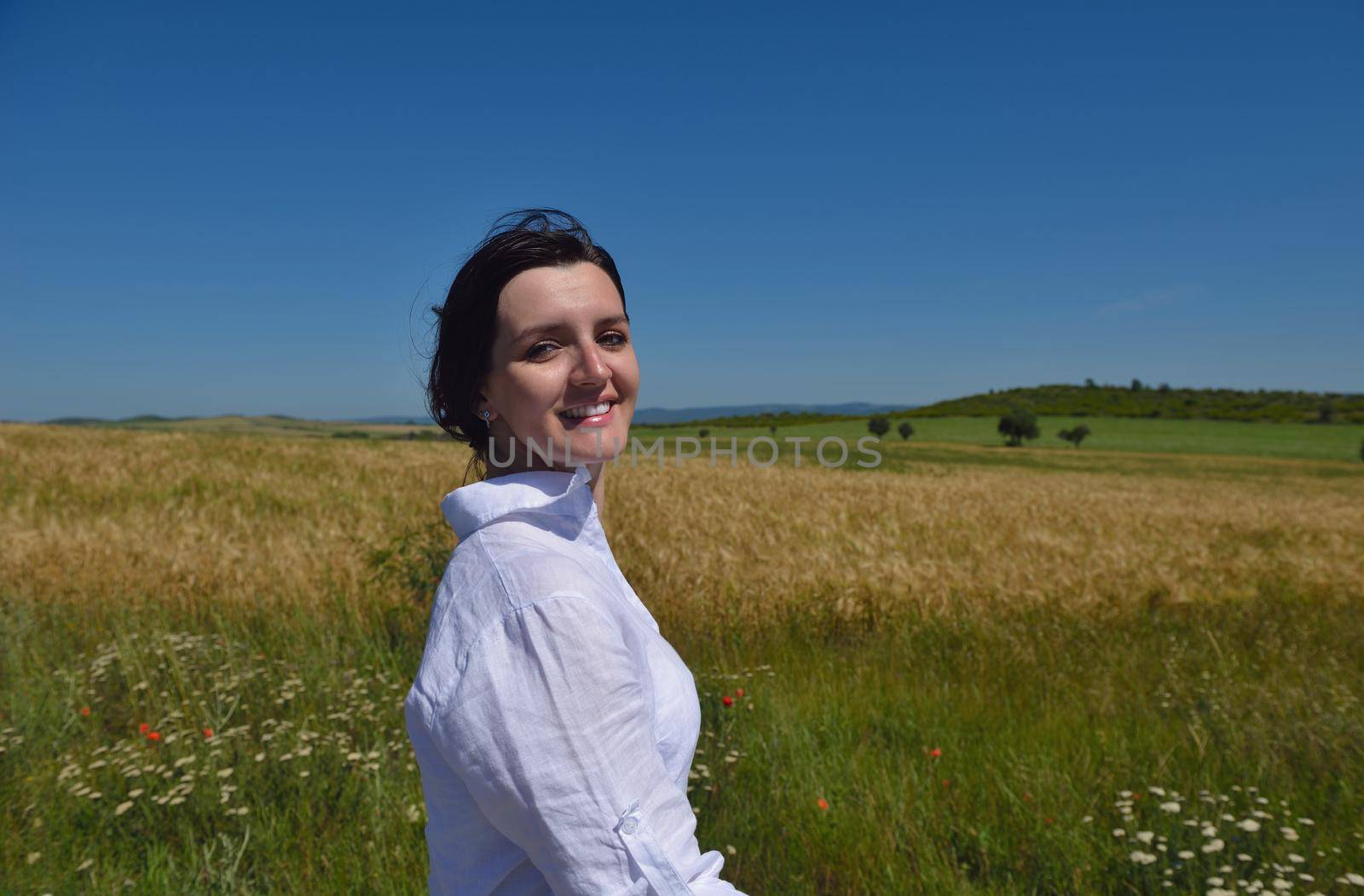 Young woman standing jumping and running  on a wheat field with blue sky in  background at summer day representing healthy life and agriculture concept