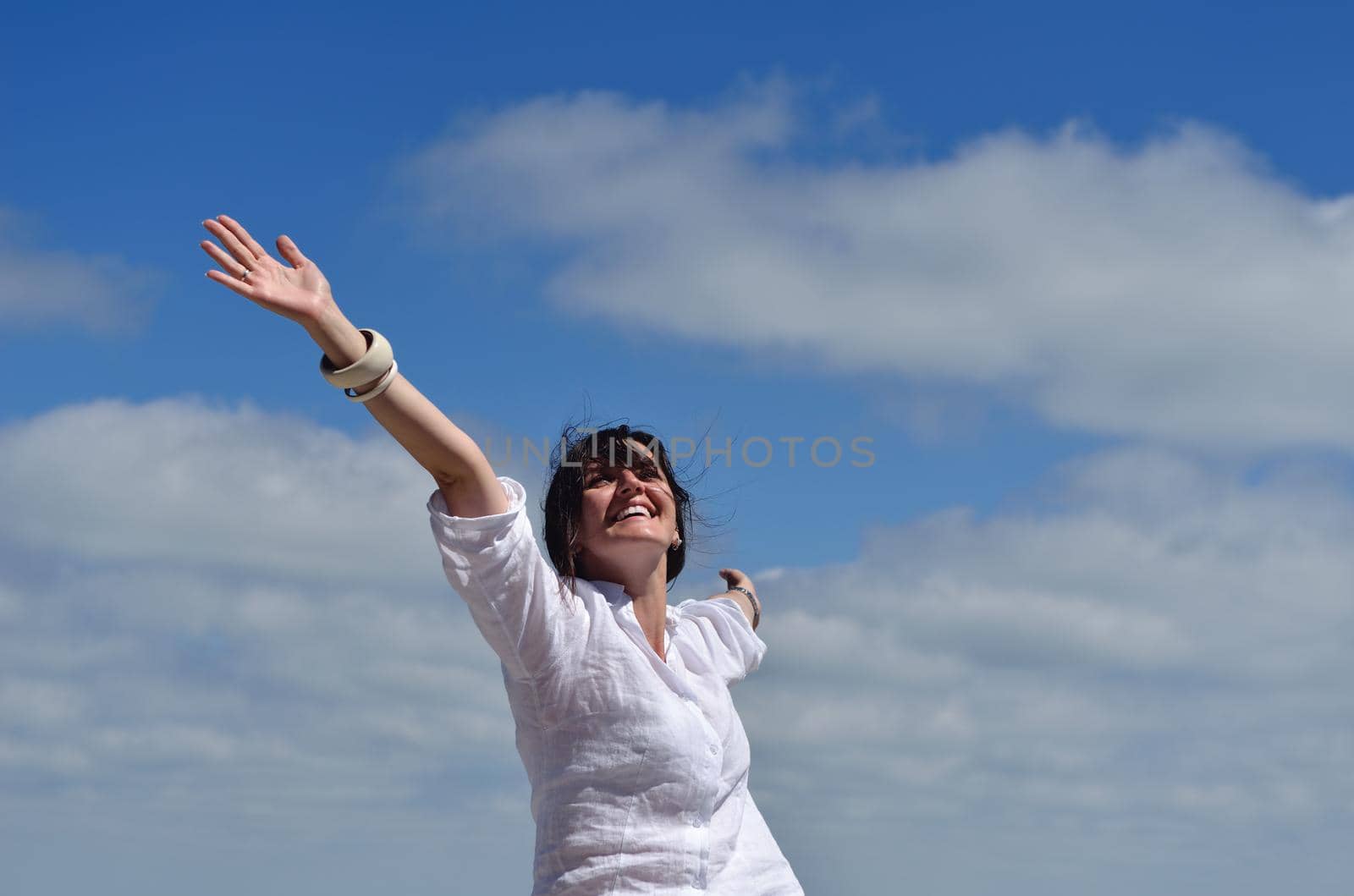 Happy  young woman with spreading arms, blue sky with clouds in background  - copyspace