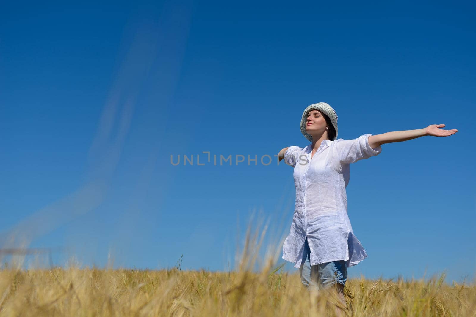 Young woman standing jumping and running  on a wheat field with blue sky the background at summer day representing healthy life and agriculture concept