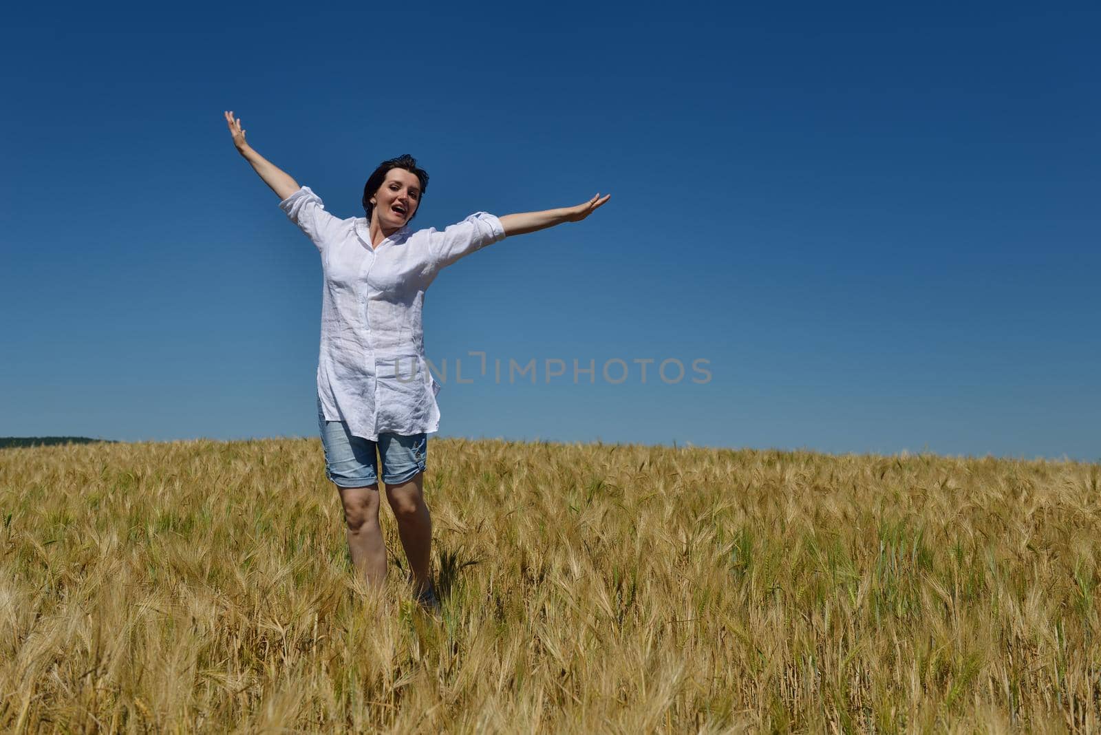 Young woman standing jumping and running  on a wheat field with blue sky the background at summer day representing healthy life and agriculture concept