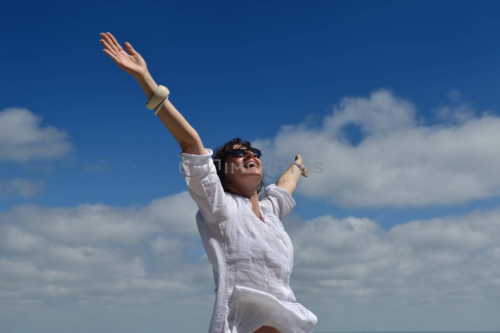 Happy  young woman with spreading arms, blue sky with clouds in background  - copyspace