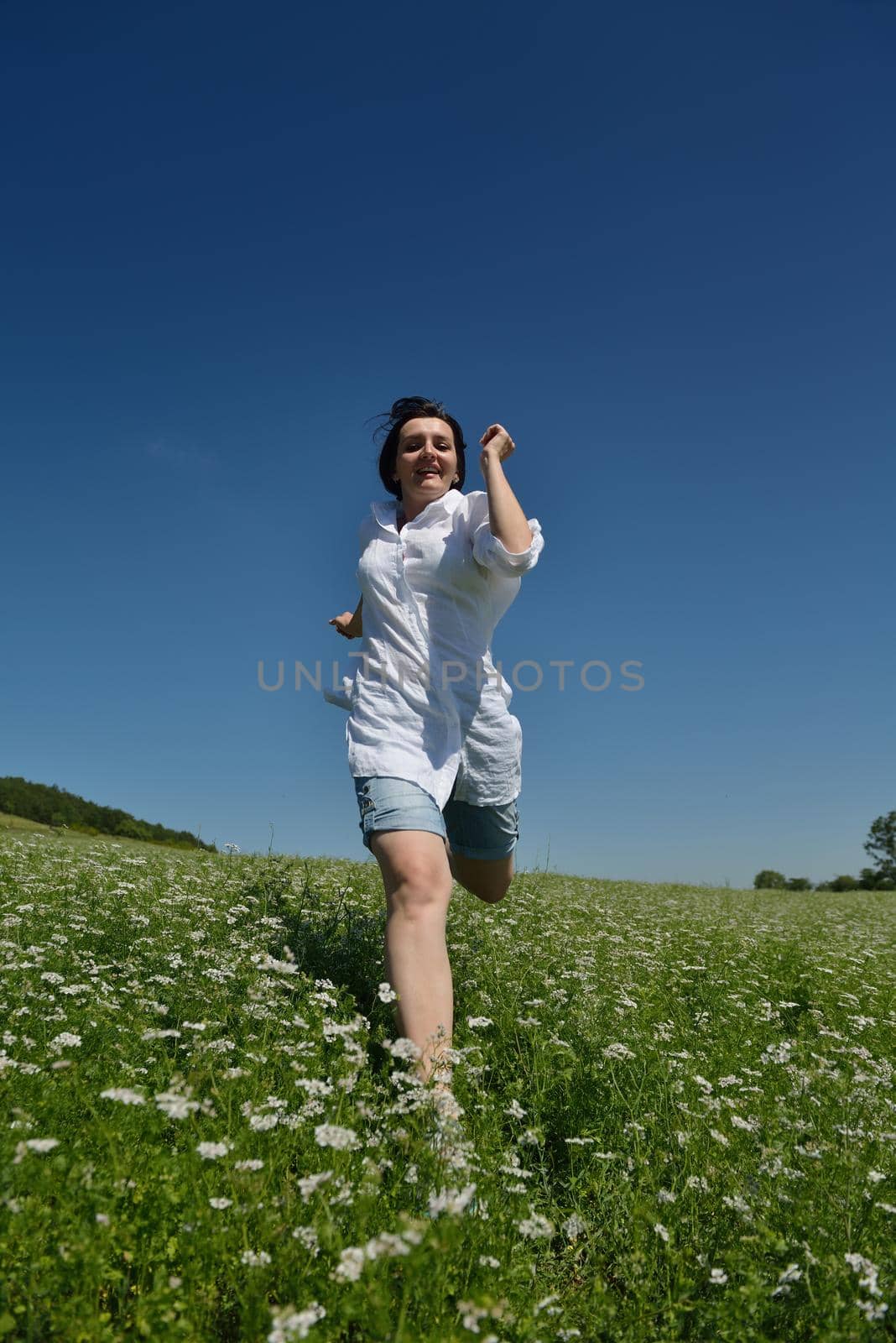 Young happy woman in green field with blue sky in background