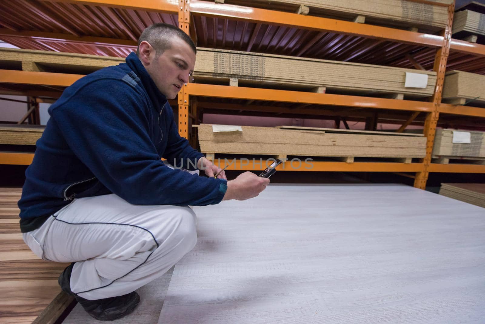 young man carpenter using a mobile phone to calculate measures for wooden board while working in big modern carpentry High quality wood concept