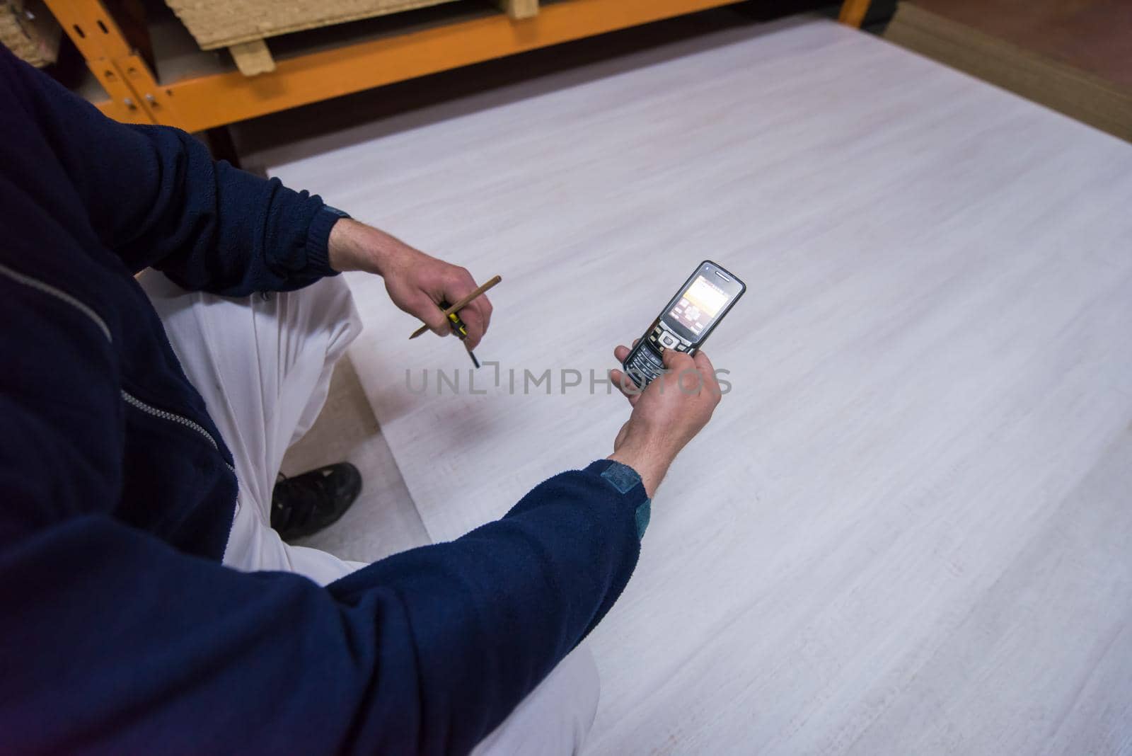 young man carpenter using a mobile phone to calculate measures for wooden board while working in big modern carpentry High quality wood concept