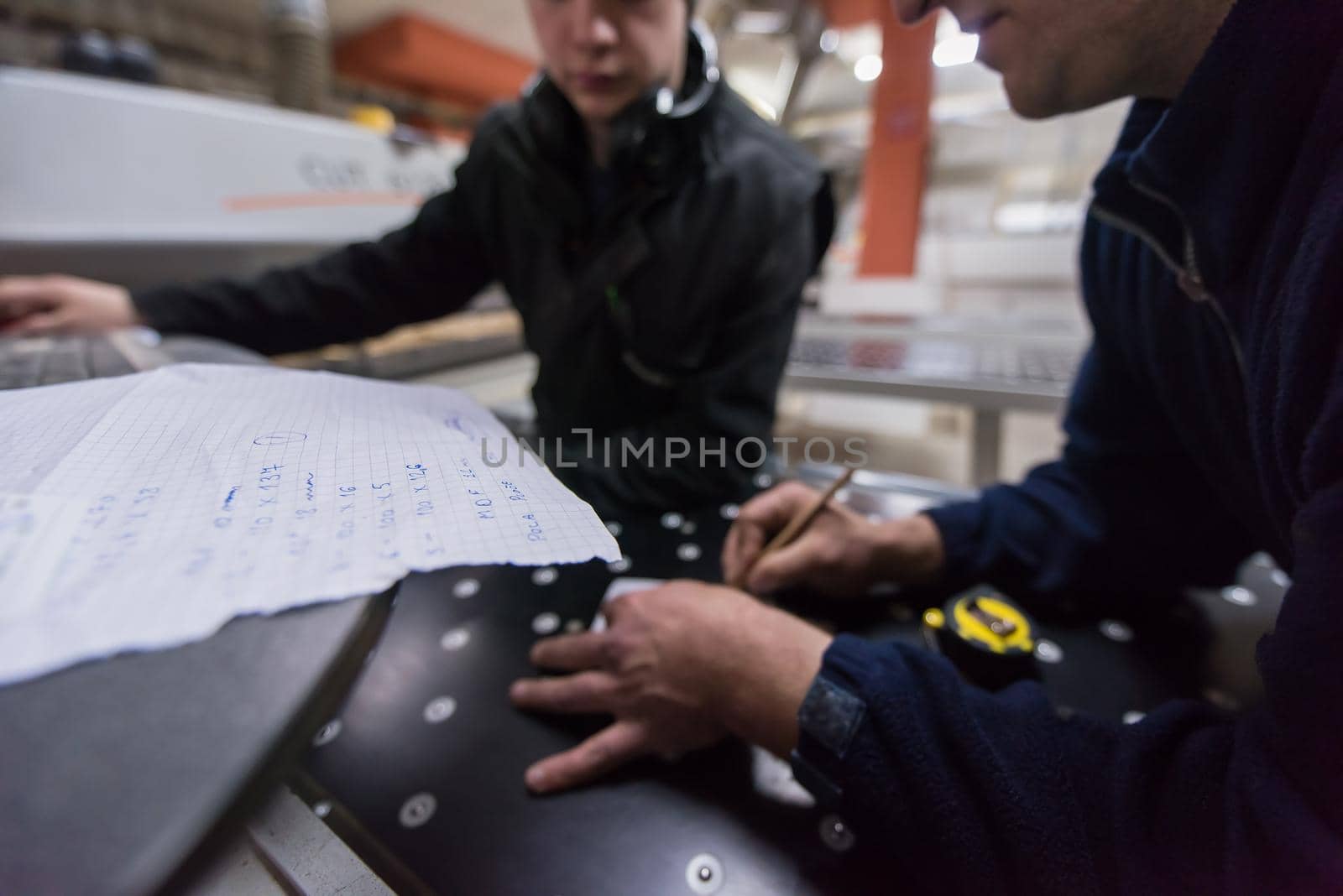 two young carpenters calculating and programming a cnc wood working machine in workshop. wood workers preparing a computer program for CNC machine at big modern carpentry