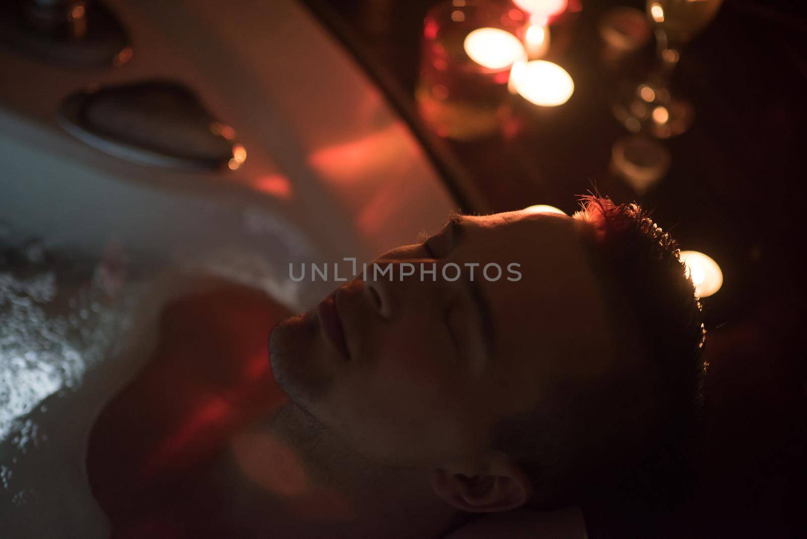 young handsome man enjoys relaxing in the jacuzzi with candles and champagne at luxury resort spa