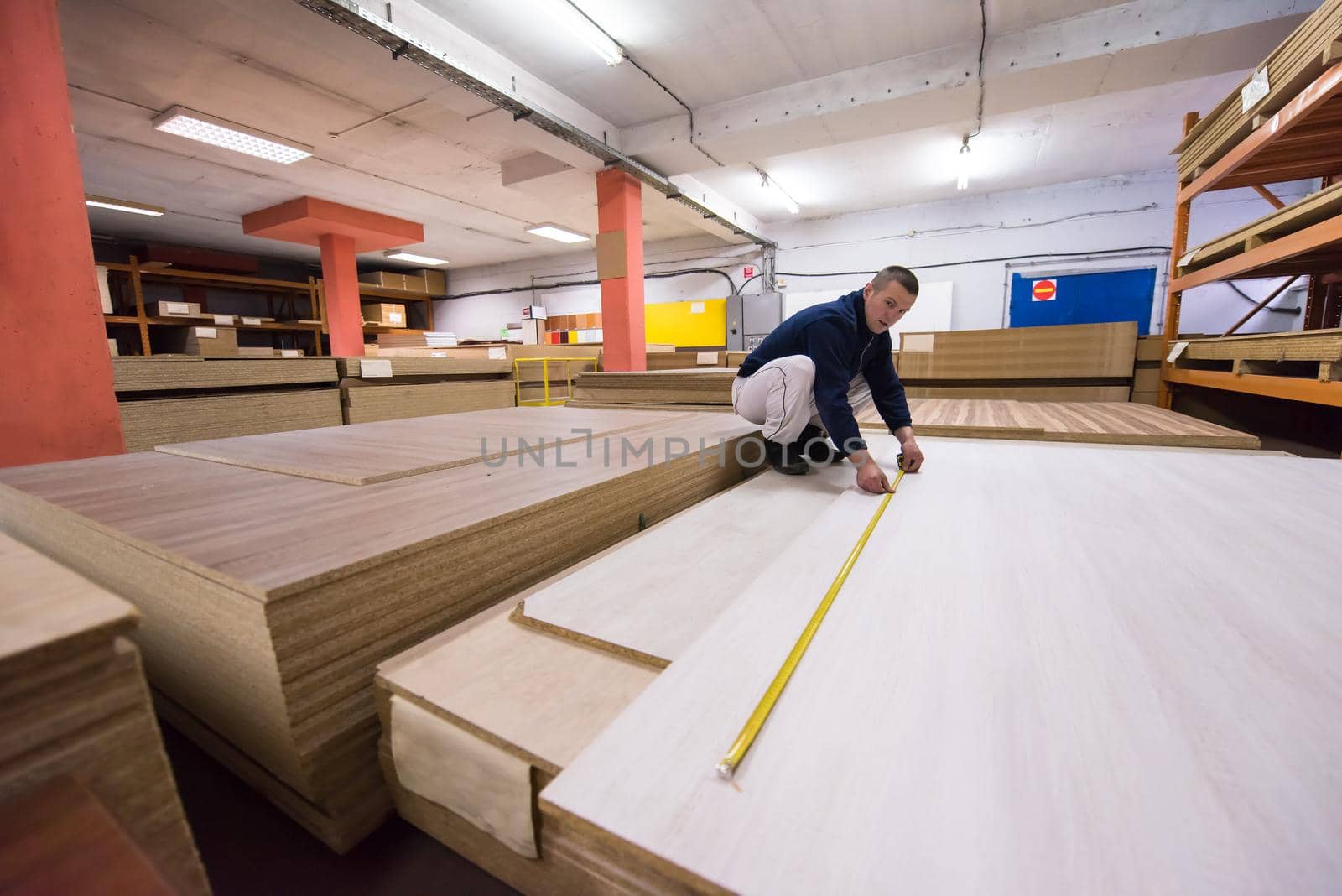 young man carpenter measuring wooden board for cutting while working in big modern carpentry High quality wood concept