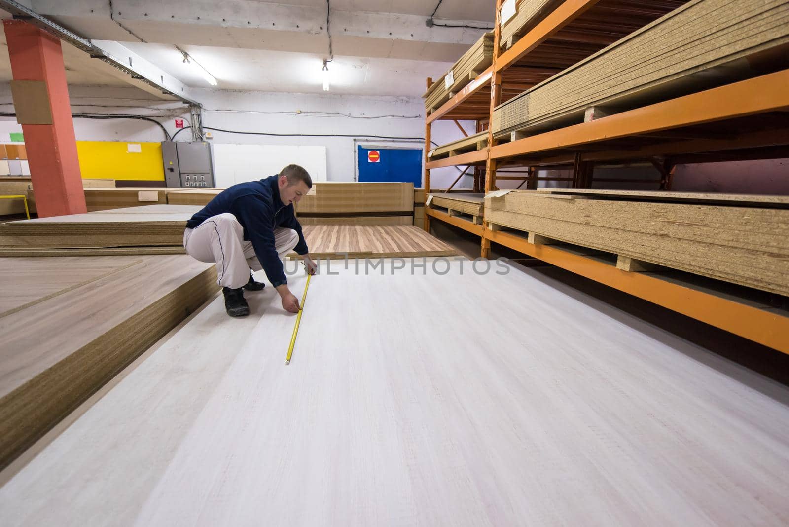 young man carpenter measuring wooden board for cutting while working in big modern carpentry High quality wood concept