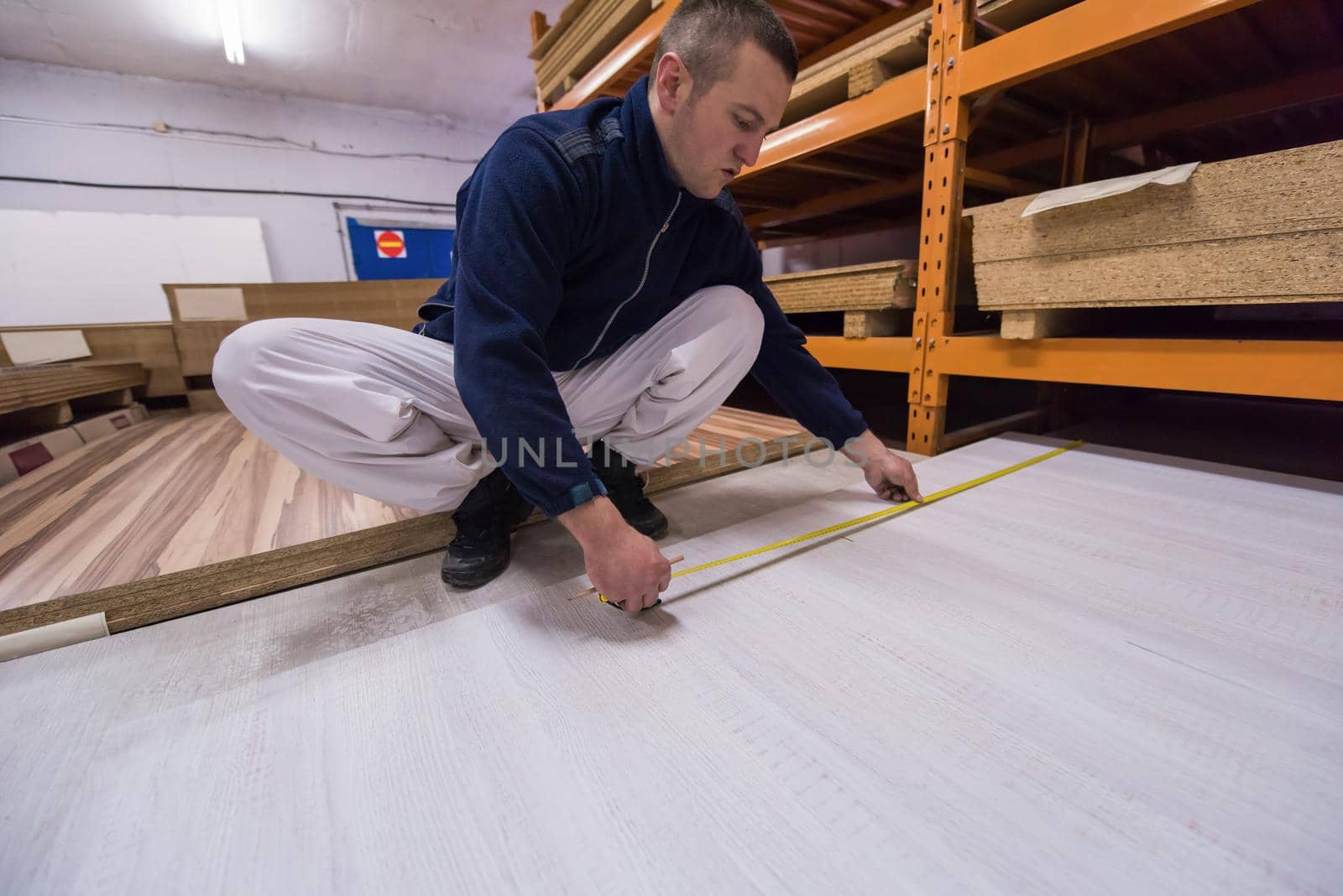 young man carpenter measuring wooden board for cutting while working in big modern carpentry High quality wood concept