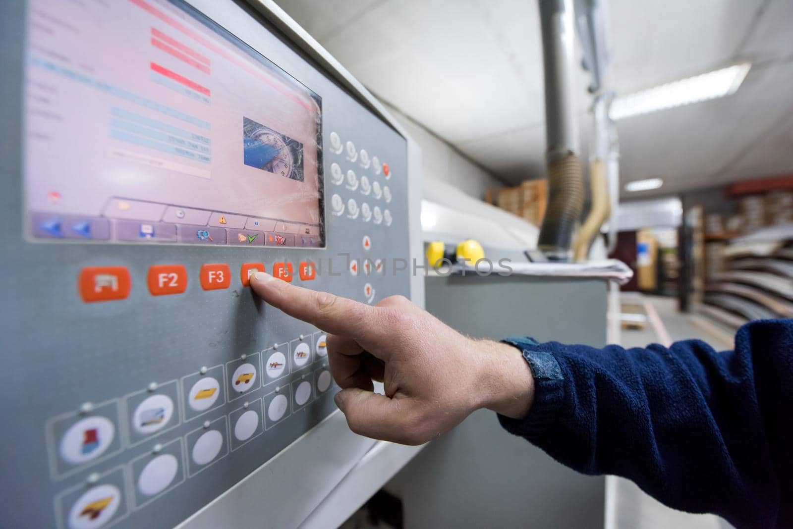 young carpenter calculating and programming a cnc wood working machine in workshop. wood worker preparing a computer program for CNC machine at big modern carpentry