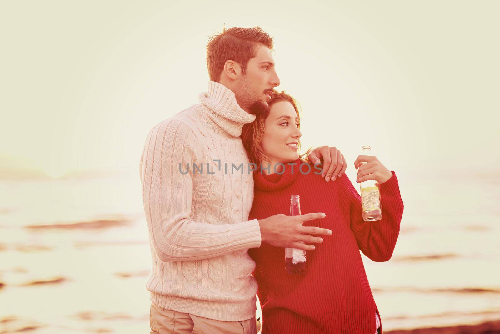 young couple hugging and drinking beer on sunset
 during autumn time at beach filter