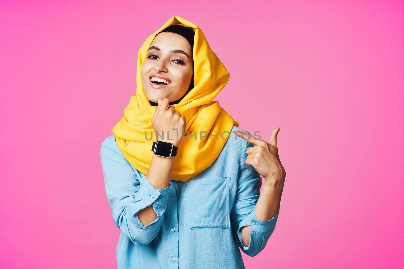 woman wearing yellow hijab electronic watch technology pink background. High quality photo