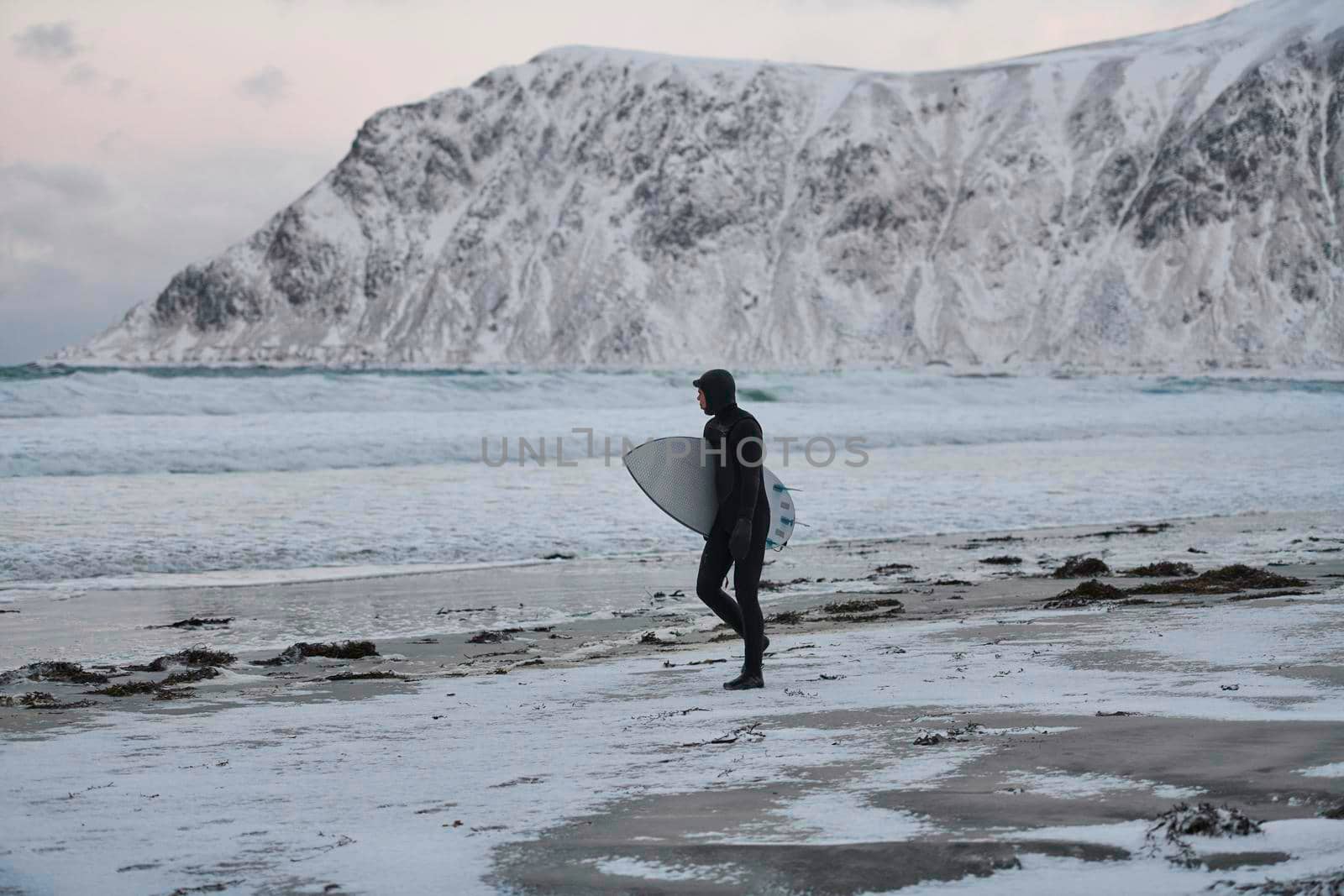 Authentic local Arctic surfer going by beach after surfing in Northern sea. Norwegian sea coastline. Winter water activities extreme sport