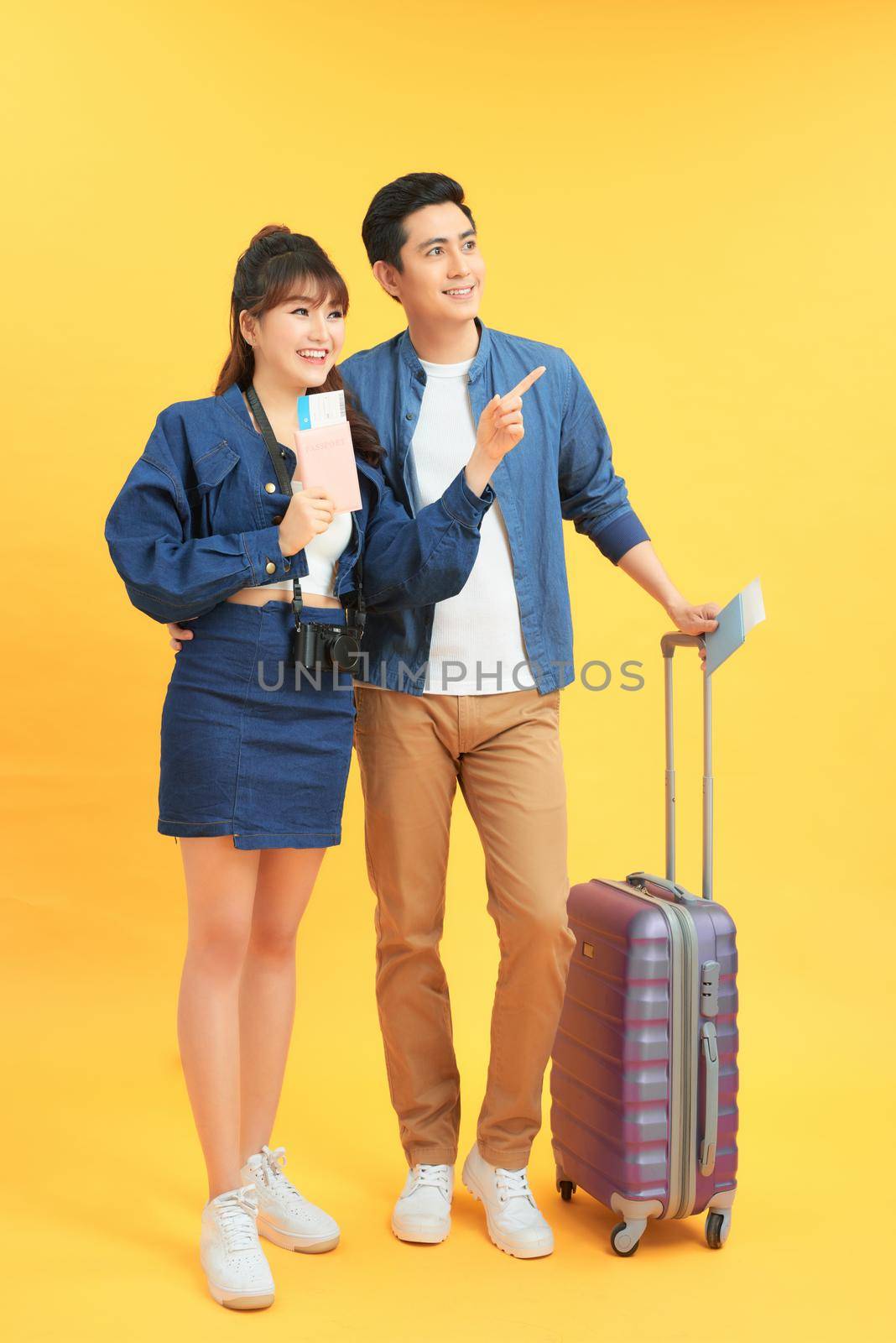 Young couple with suitcases on yellow background