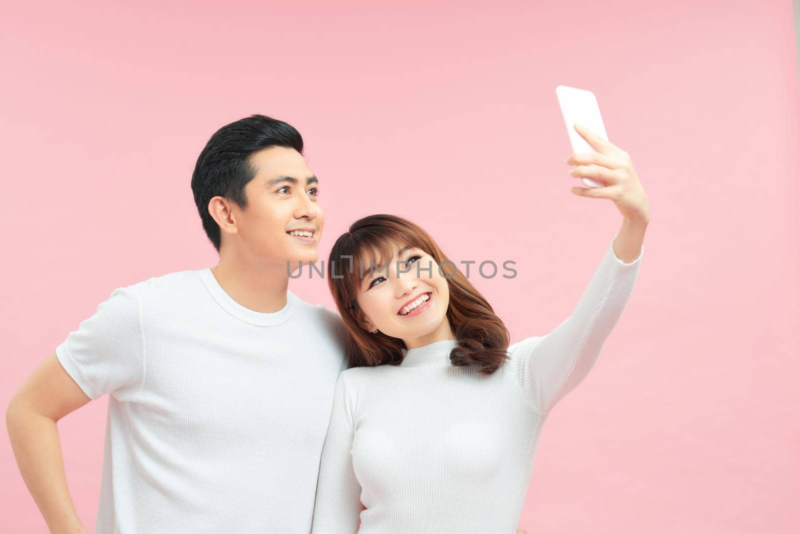 Happy young couple makes selfie, dressed in stylish clothes on pink background