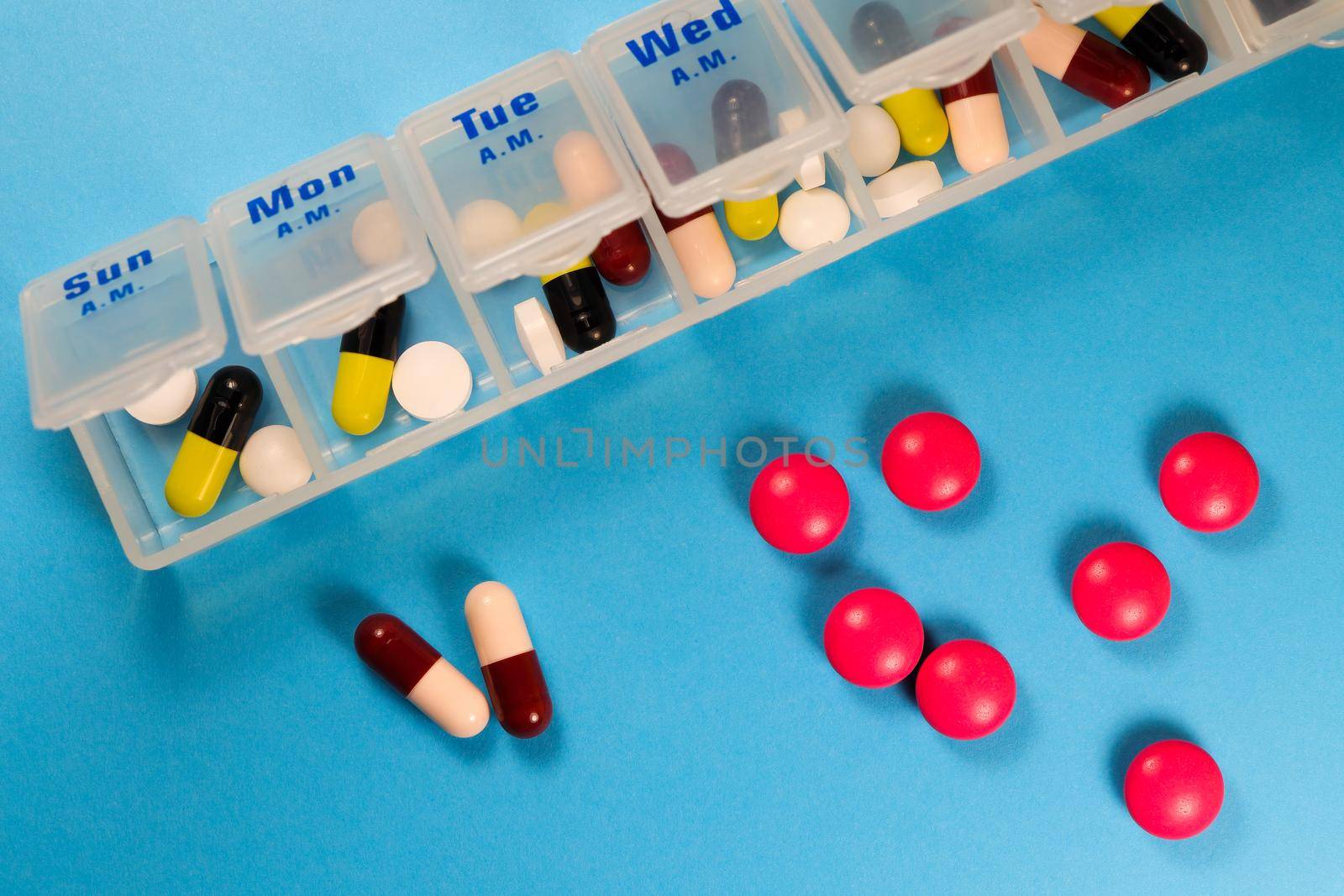 Pill and capsule medicine schedule sorting tray on blue background flat-lay