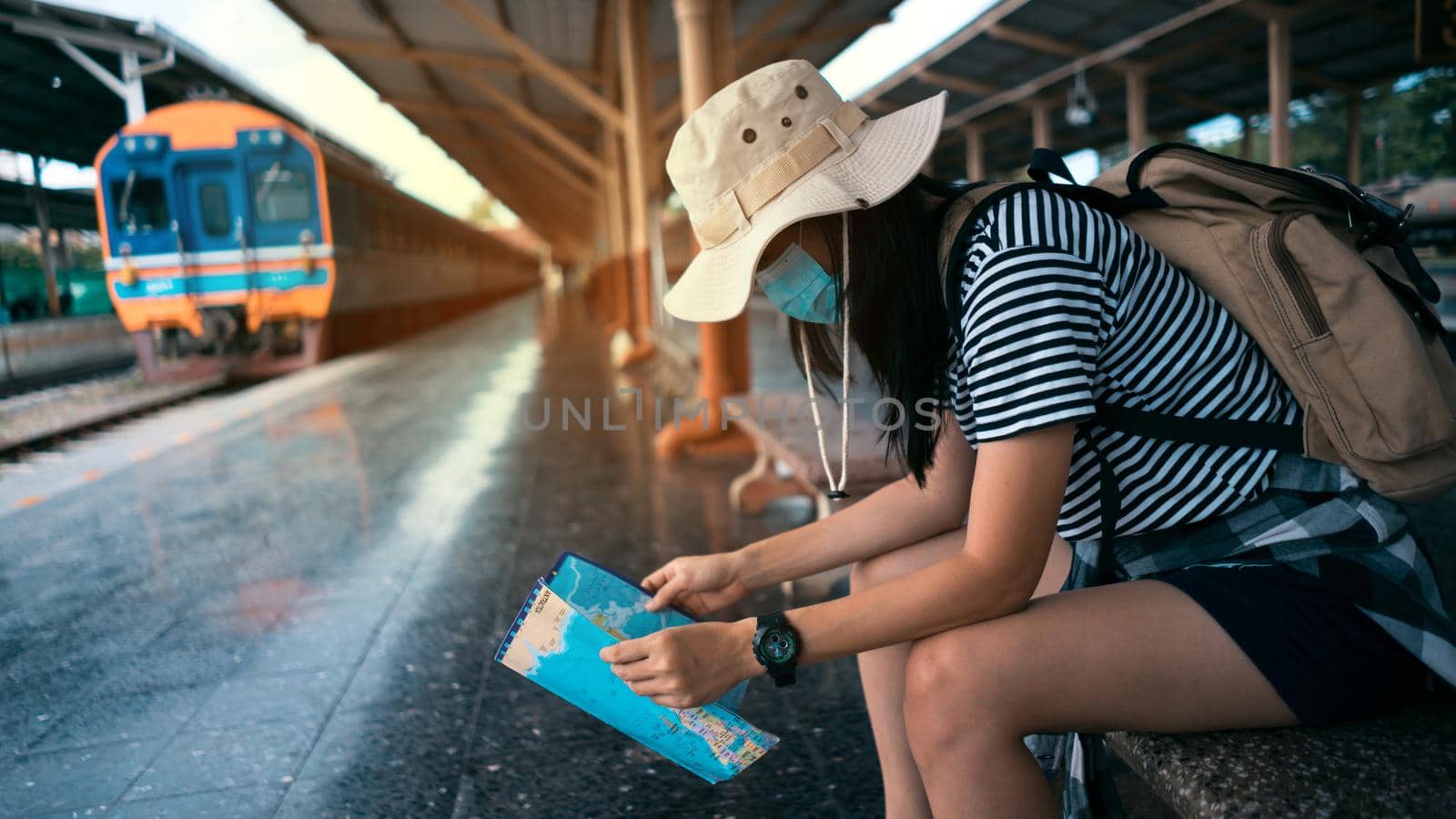 New normal traveler concepts. Young female tourist wearing a mask looks at a tourist map while waiting for a train at the train station. by pravinrus