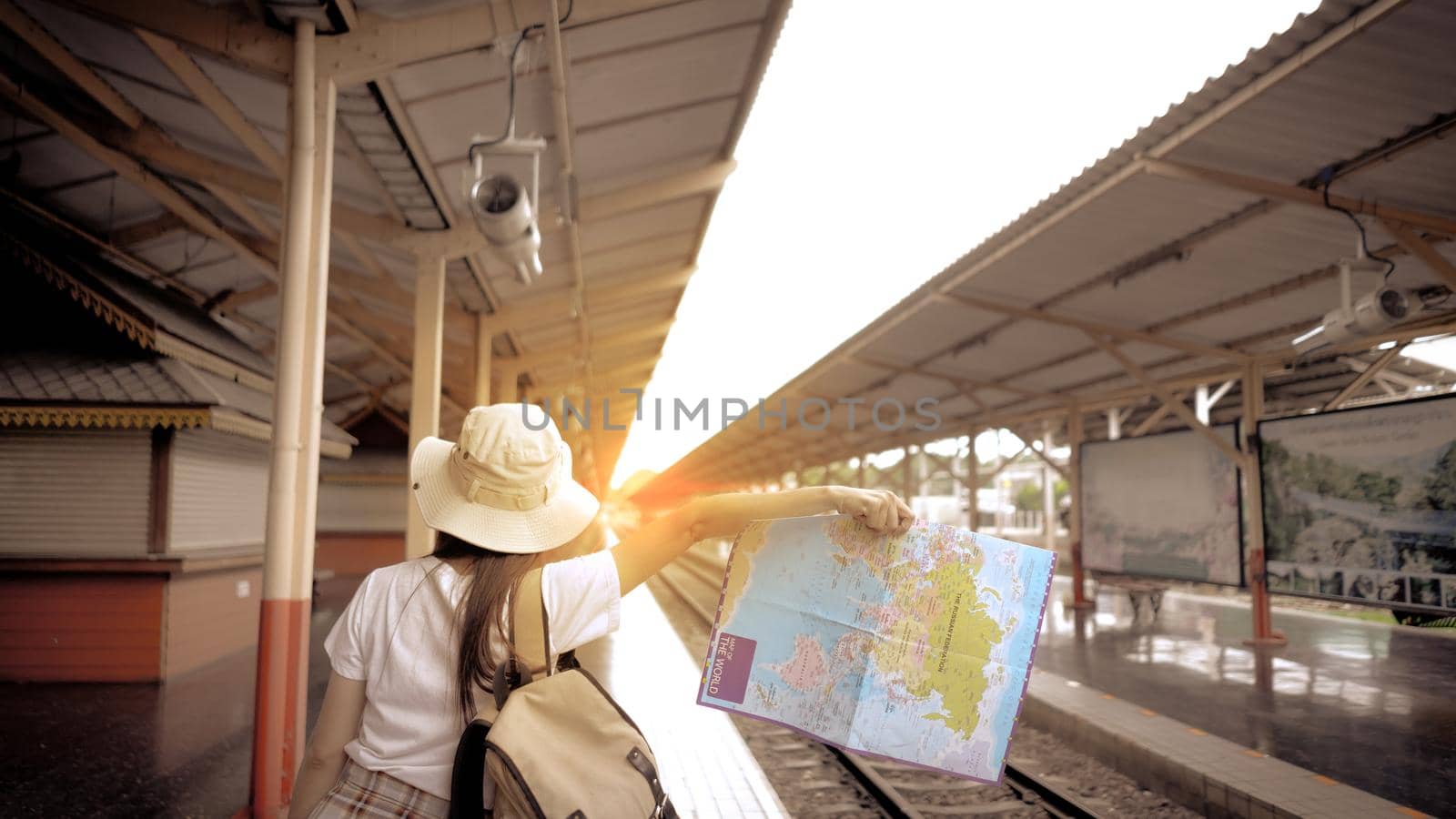 Young Girl Tourist carrying a bag and holding map hitchhiking the train on the railway at the train station. Concept of travel and tourism.