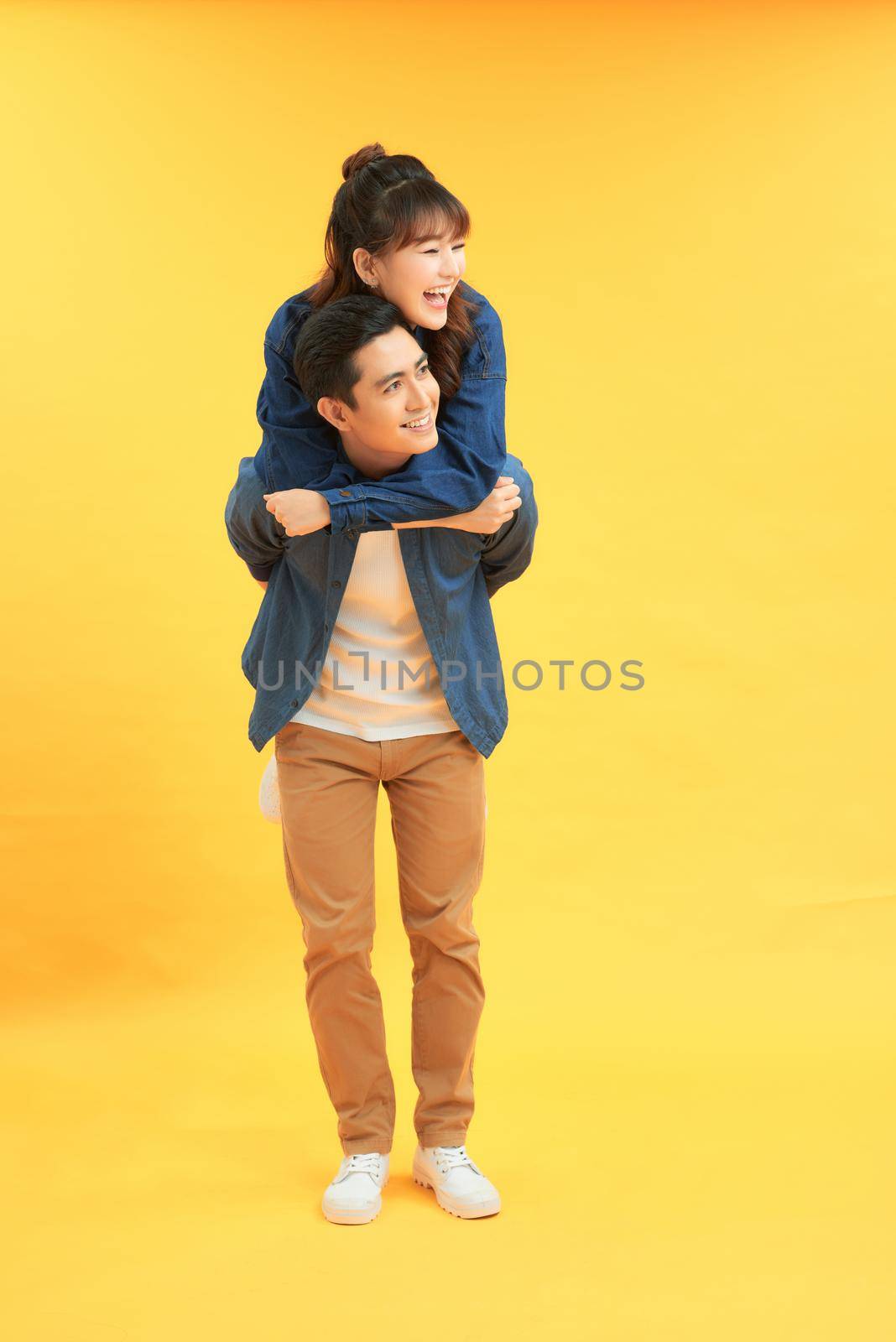 Happy man carrying his girlfriend on the back on yellow background by makidotvn