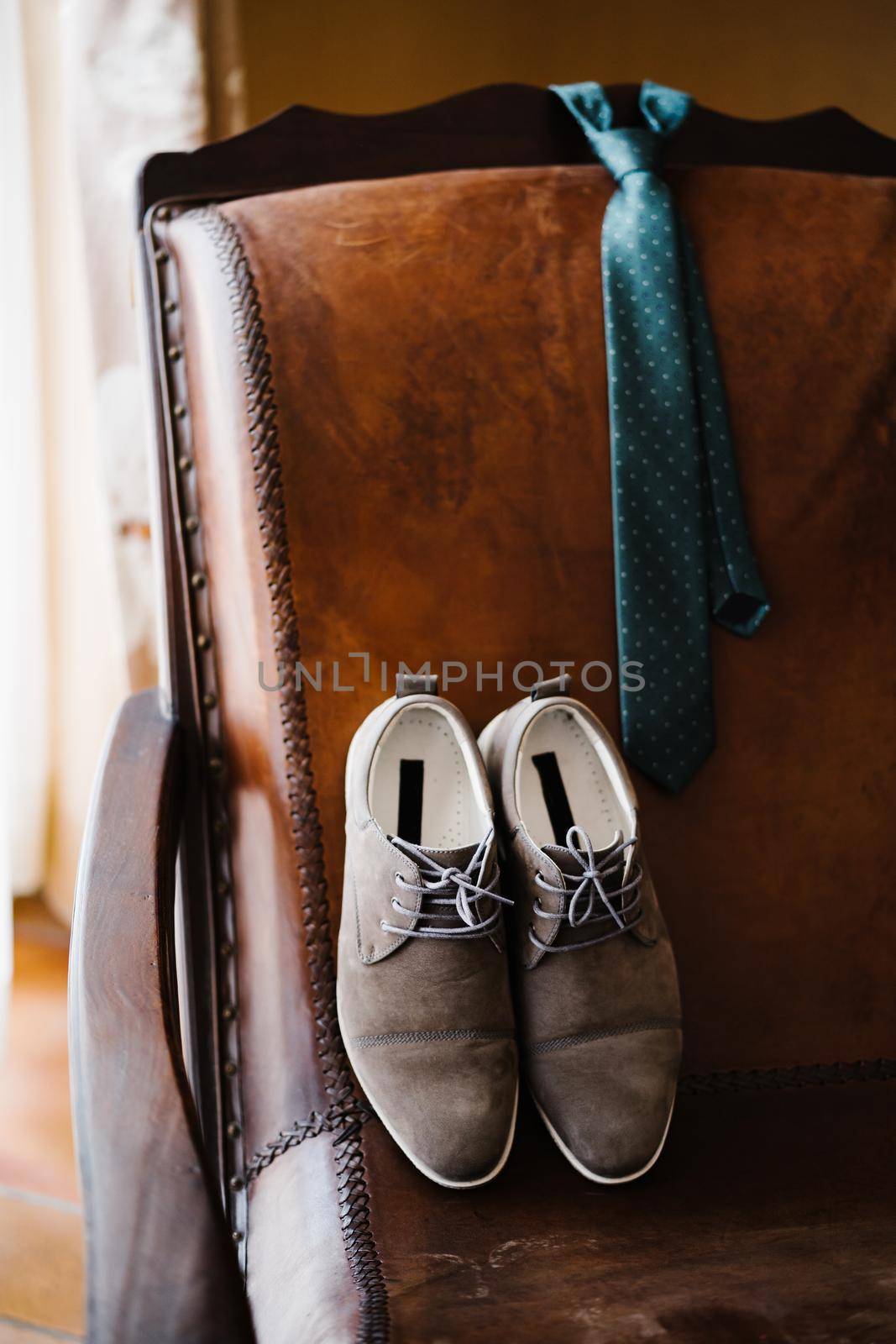 Groom's shoes and polka dot tie on a leather chair in the room. High quality photo