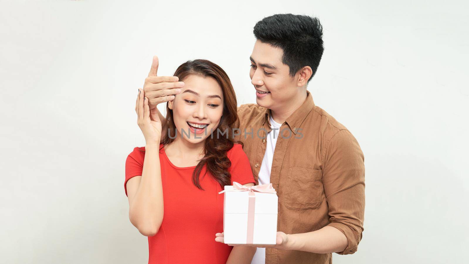 Surprised young couple isolated on white background. Valentine's Day Women's Day, birthday, holiday concept. Hold red present box with gift ribbon bow by makidotvn