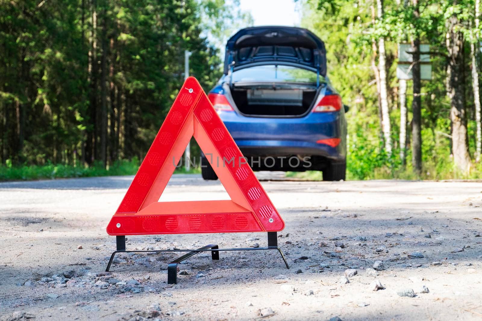 Close-up of a portable reflective red warning triangular sign on the side of a rural road near a car. Selective focus.