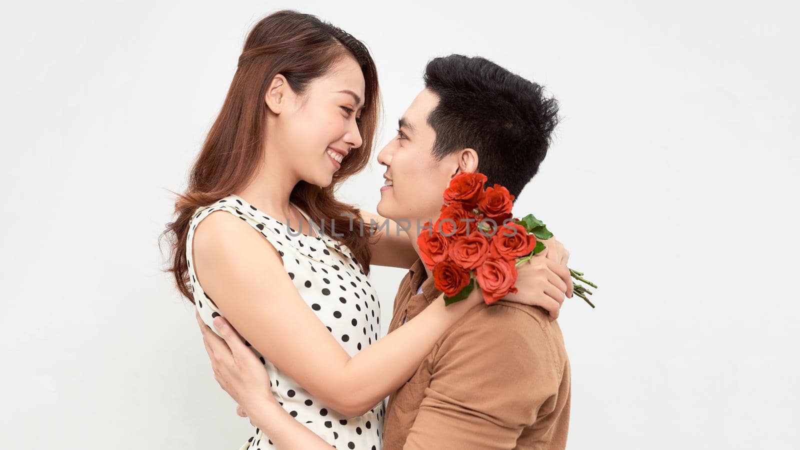 Elegant couple of young lovers holding hands, a girl holding a large bouquet of red roses.