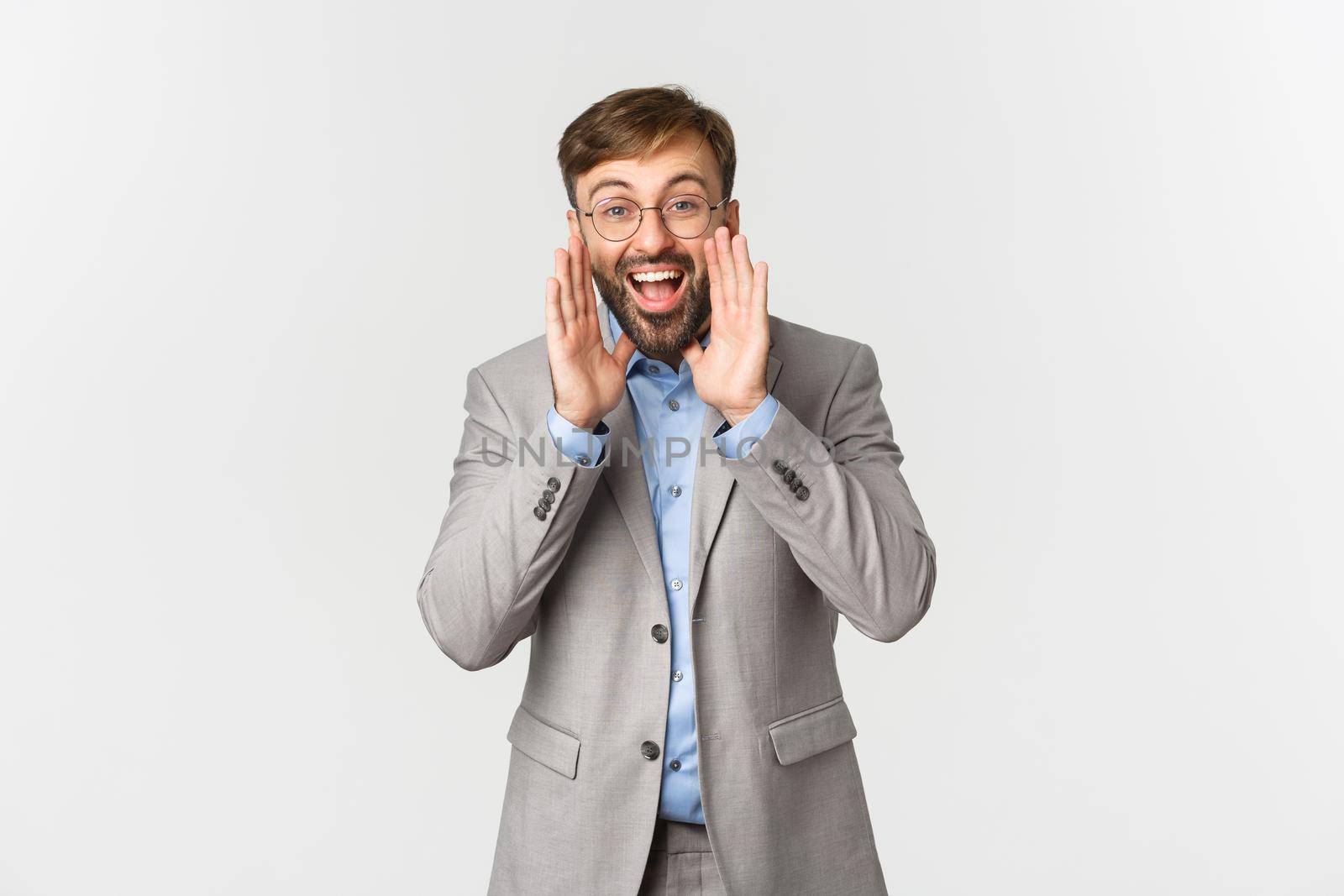 Portrait of happy businessman in grey suit and glasses, making announcement, shouting loud and searching for employees, standing over white background by Benzoix