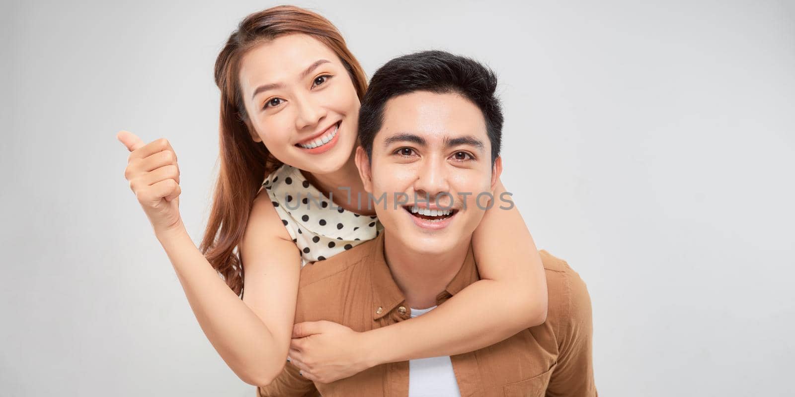 Love forever. Young asian handsome boyfriend is piggybacking his cute lover, wearing casual clothes, on white background by makidotvn