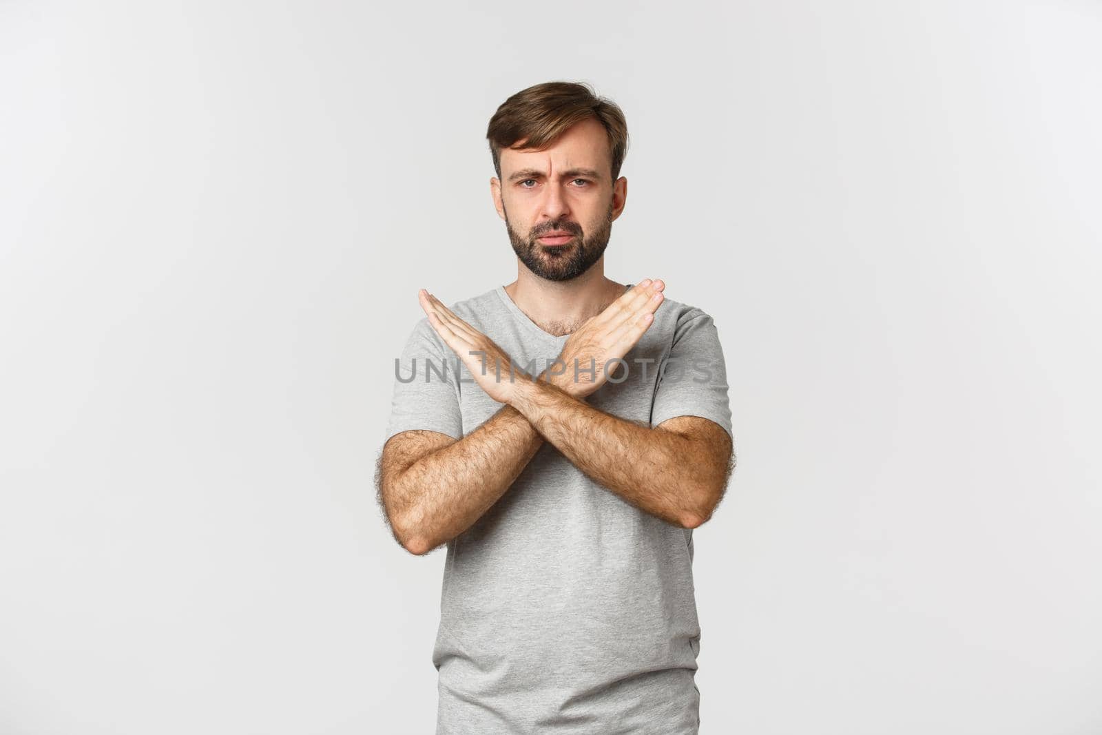 Disappointed man with beard, showing cross gesture and frowning, telling to stop, prohibit something bad, standing over white background.