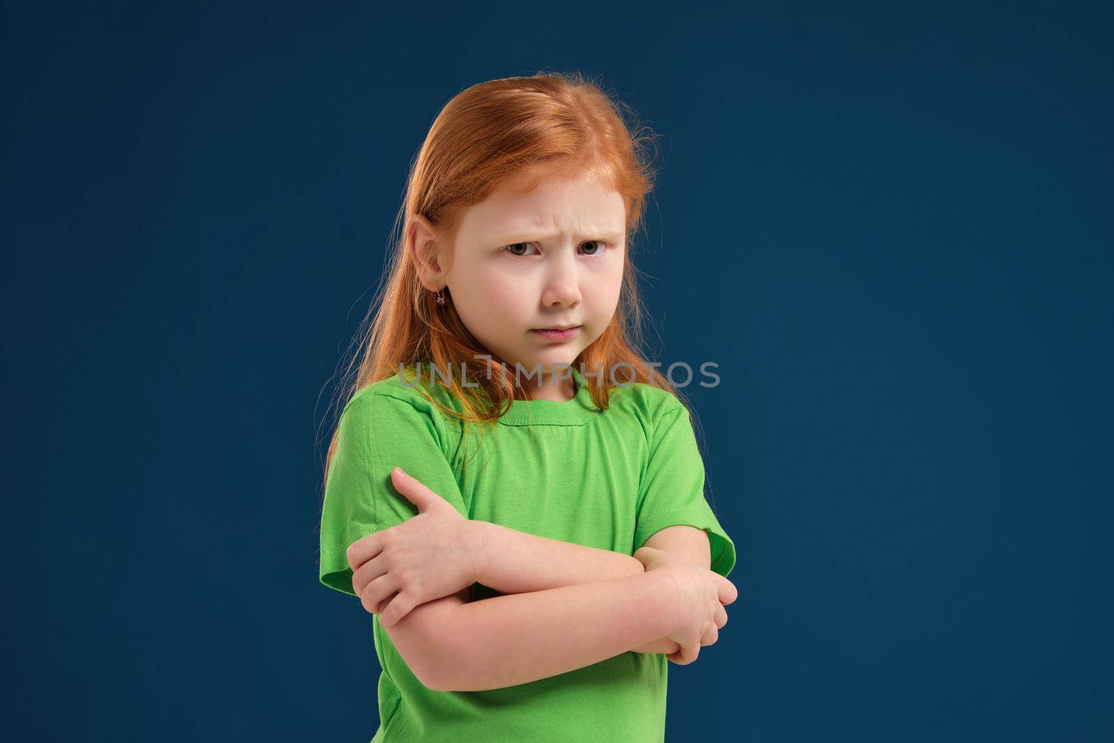 close up photo of little redhead emotional girl in green t-shirt posing before camera. She shows mistrust and shyness