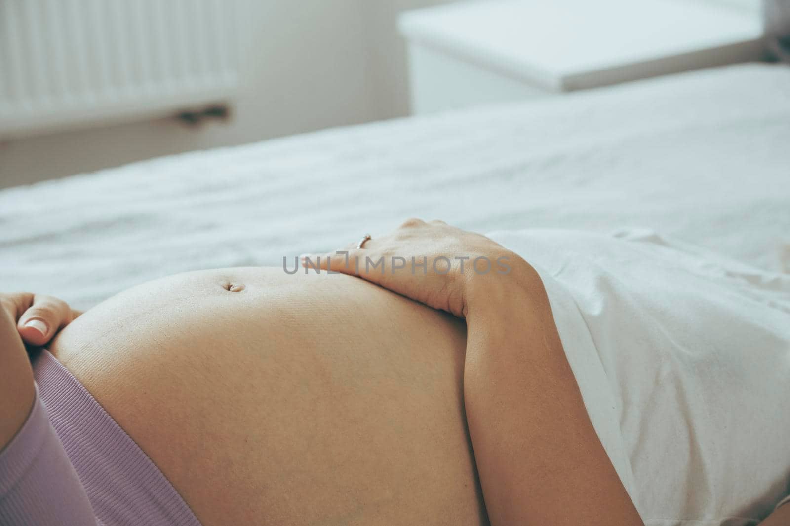 Pregnant caucasian woman laying on a sofa with her arm at tummy, view from a side.
