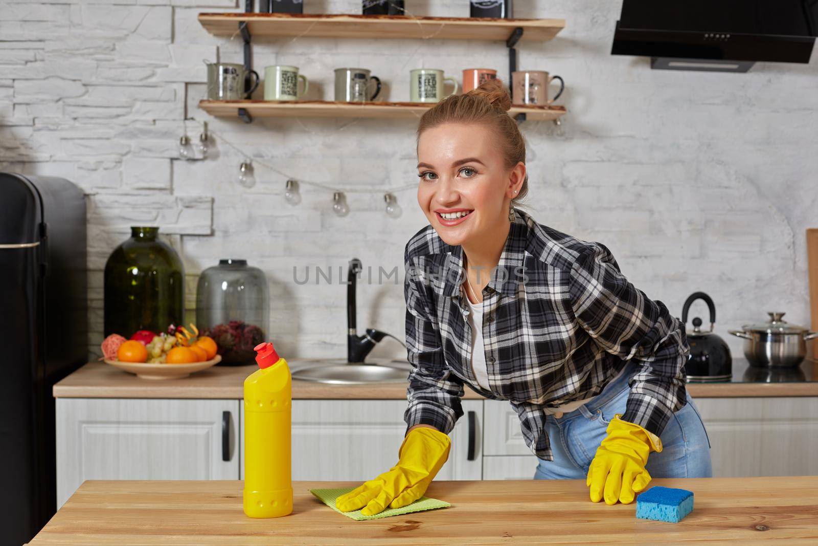 Household, cleaning and people concept - happy woman or housewife in rubber gloves wiping table with microfiber cloth at home kitchen.