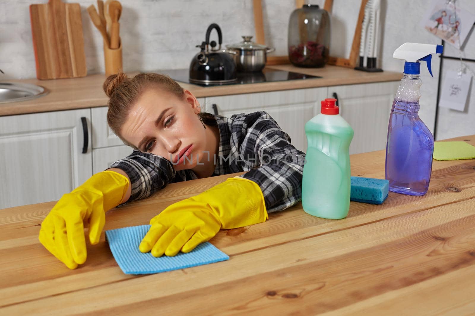 Young woman in protective gloves wipes a table in the kitchen with a rag. Fatigue. Household, cleaning and people concept