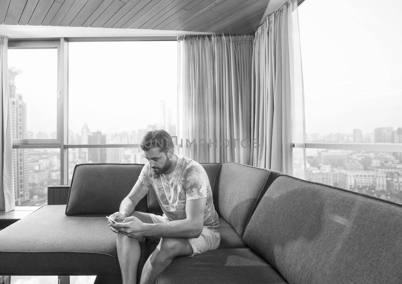 young man sitting on sofa and using a mobile phone  near the window at home