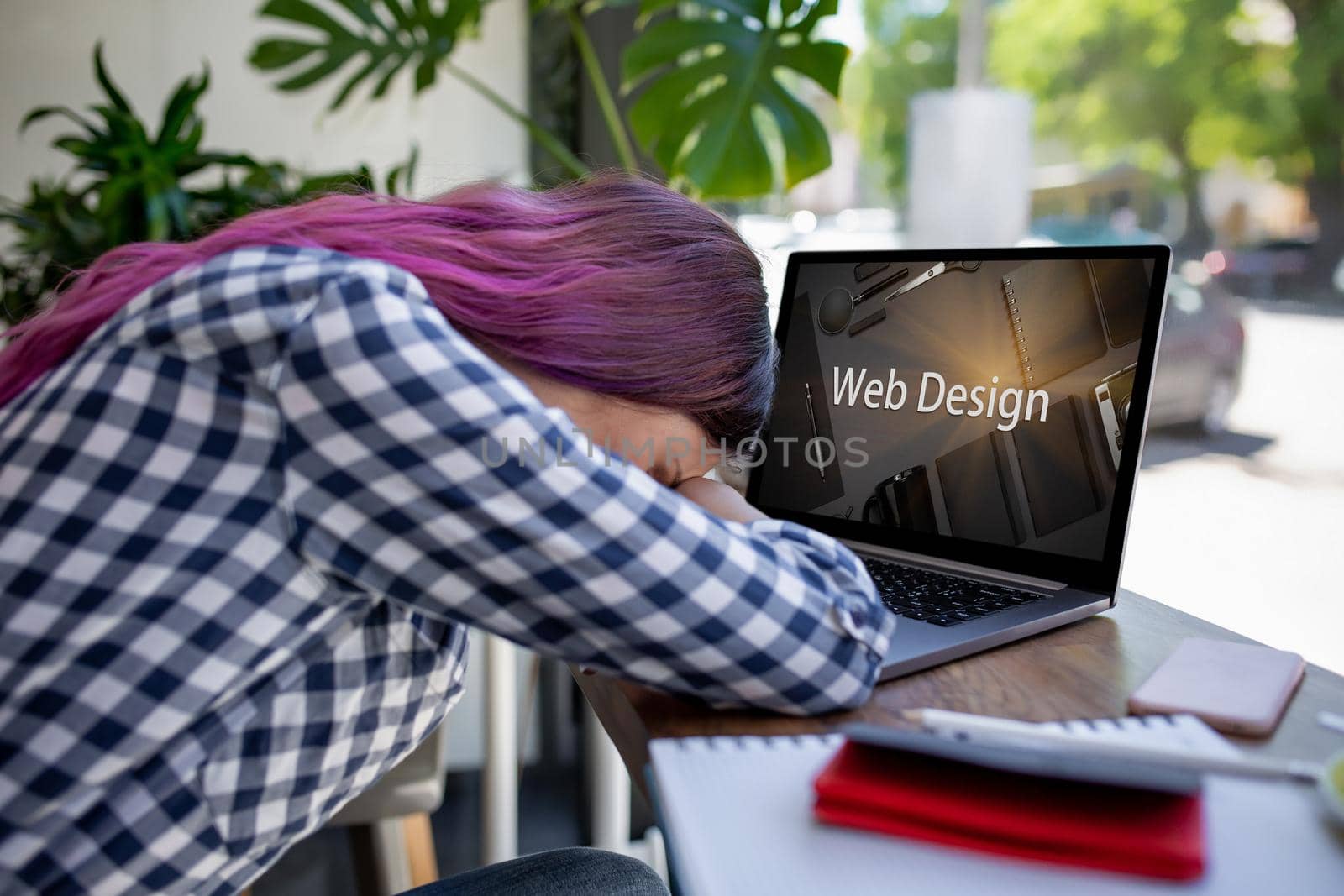 Cropped shot view of young woman working on laptop computer while sitting in modern cafe bar interior, pink hair female freelancer using net-book for remote job during morning breakfast in coffee shop. Design. Web design