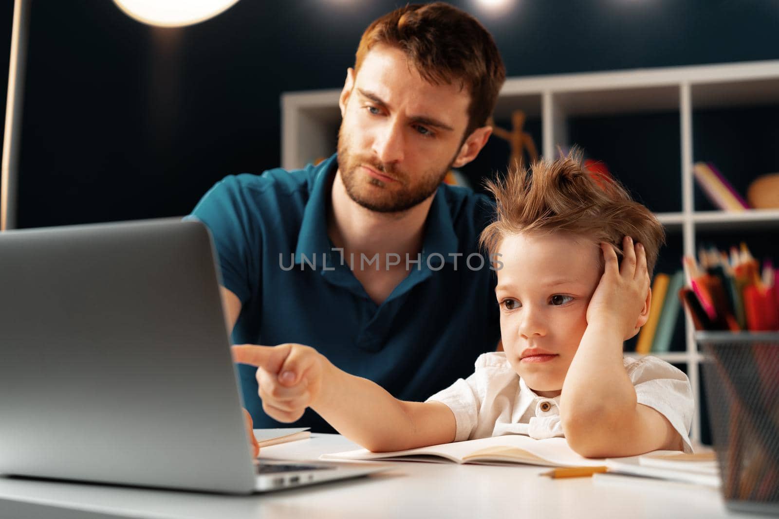 Young boy sitting with his father at the table and using laptop for study