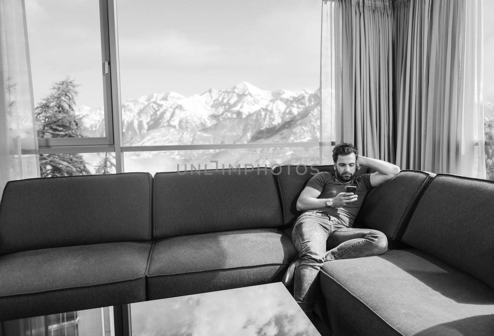 young man sitting on sofa and using a mobile phone  near the window at home