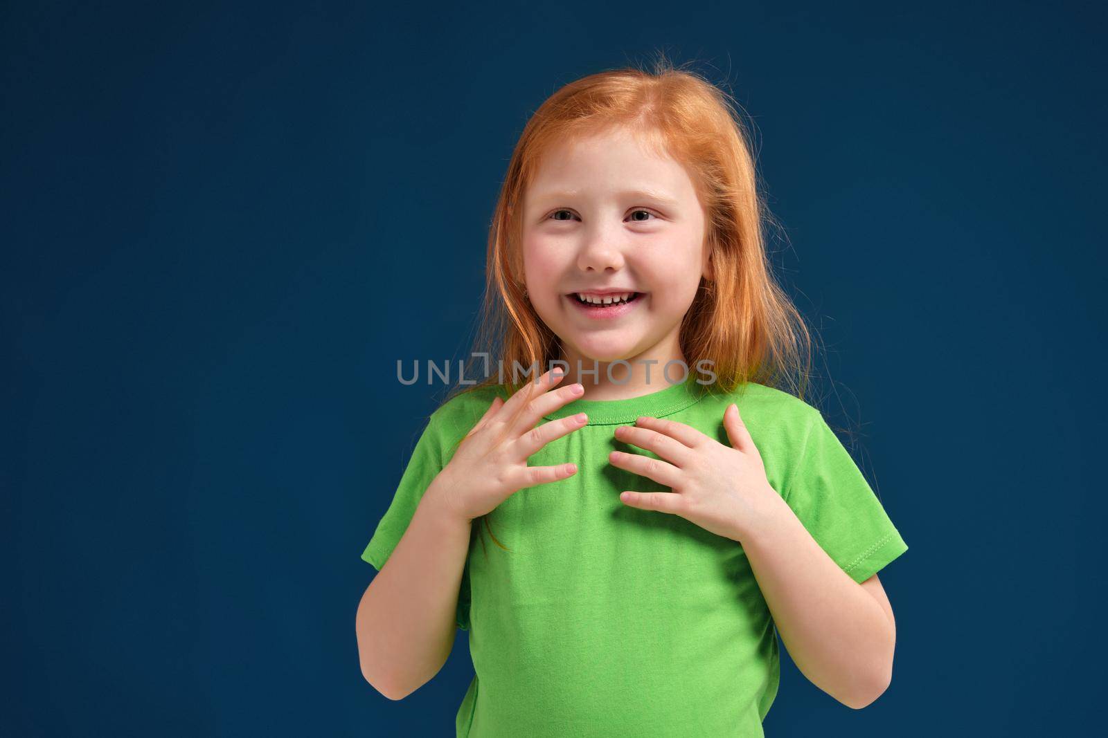 Cute little girl, in green t-shirt surprised by something, she feels emotional lift, blue background