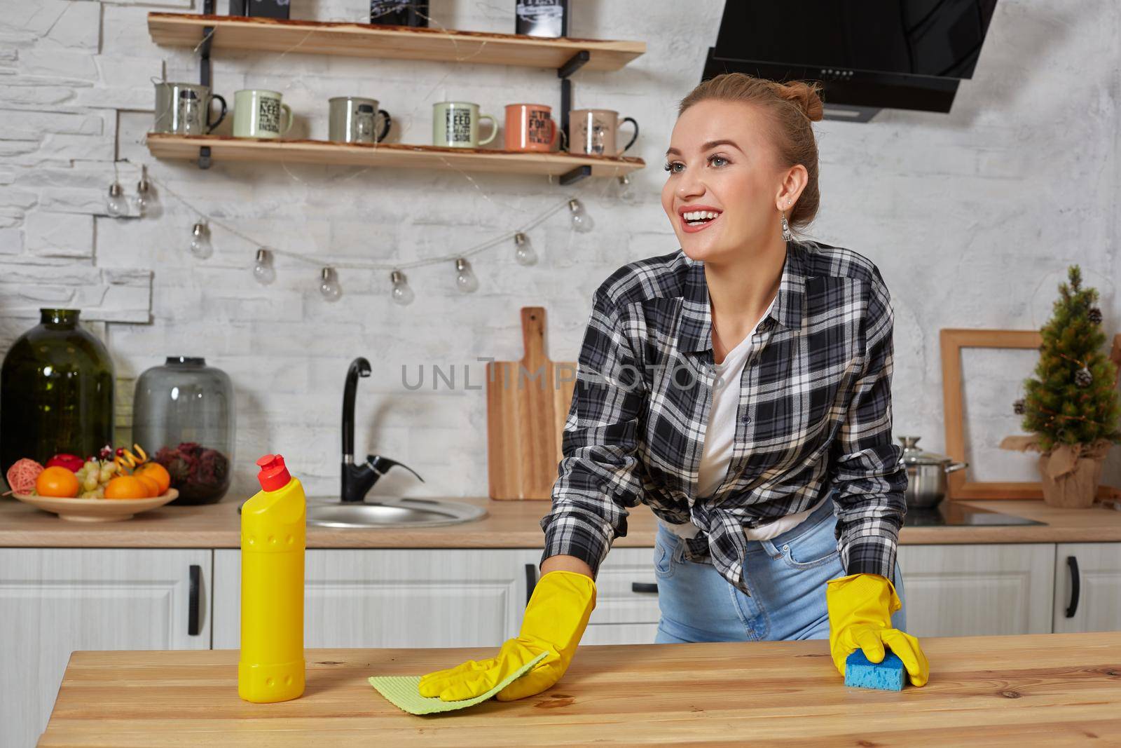 Household, cleaning and people concept - happy woman or housewife in rubber gloves wiping table with microfiber cloth at home kitchen.
