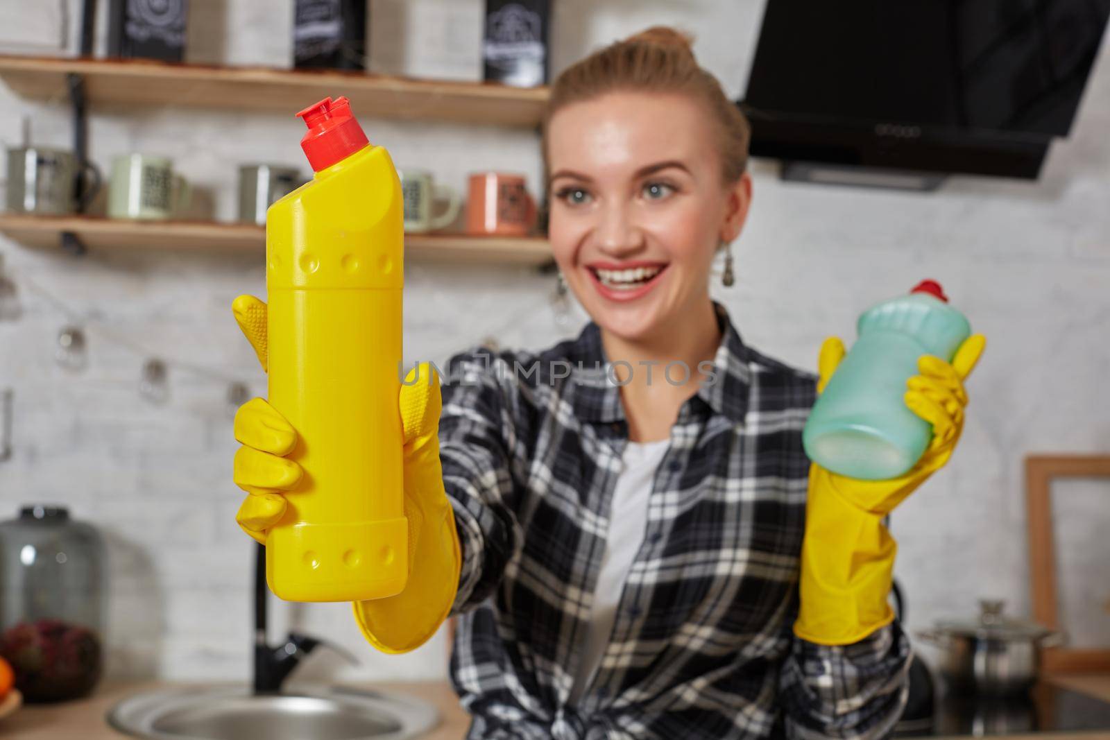 Woman comparing detergent products, she is holding two bottles and checking them at home kitchen. Household, cleaning and people concept