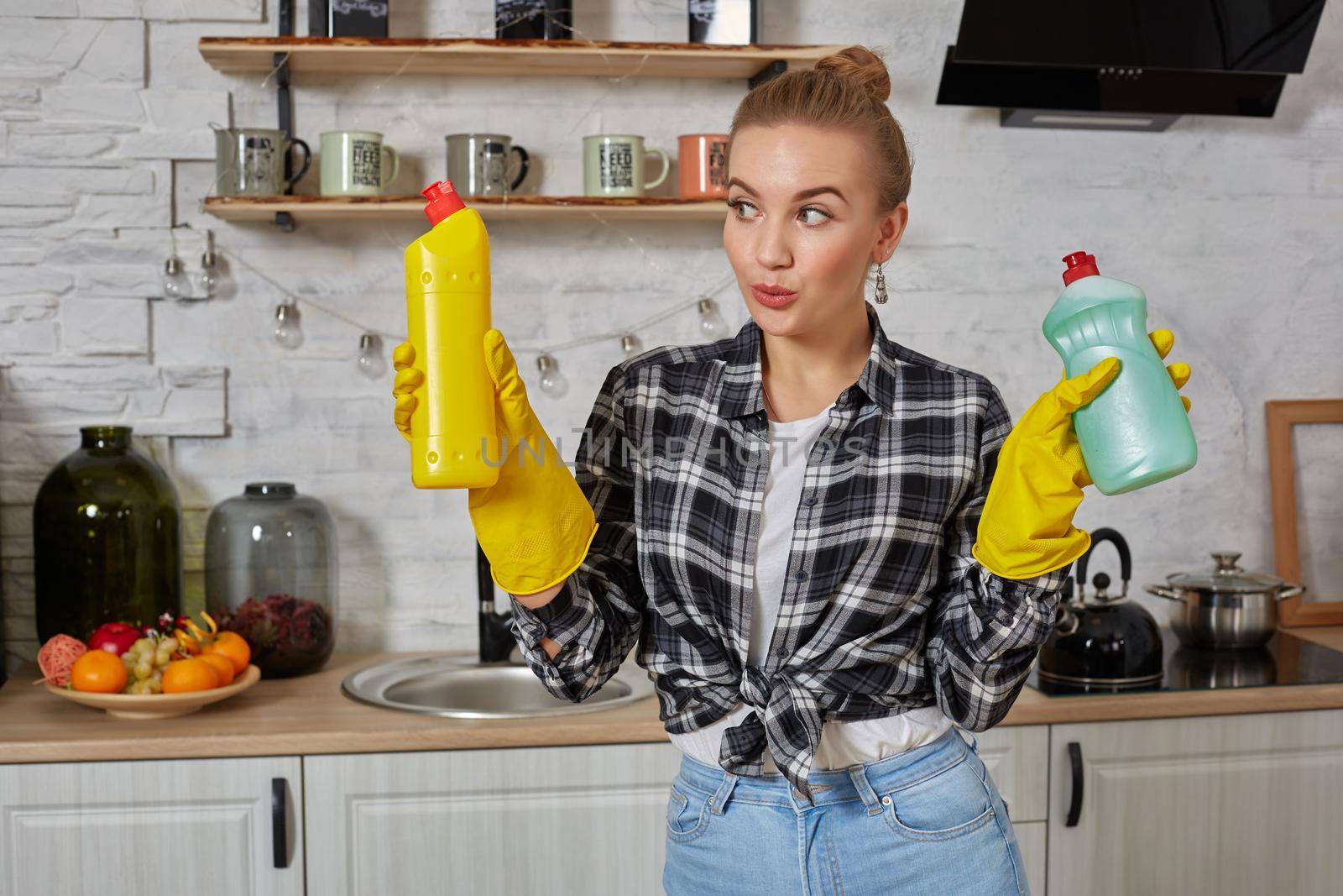 Woman comparing detergent products, she is holding two bottles and checking them at home kitchen. Household, cleaning and people concept