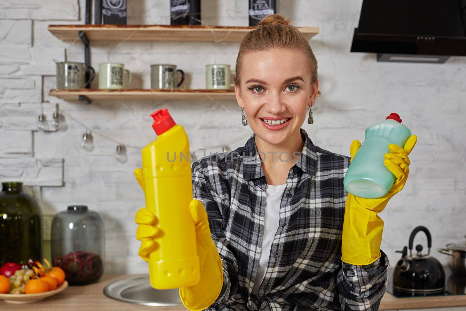 Woman comparing detergent products, she is holding two bottles and checking them at home kitchen. Household, cleaning and people concept