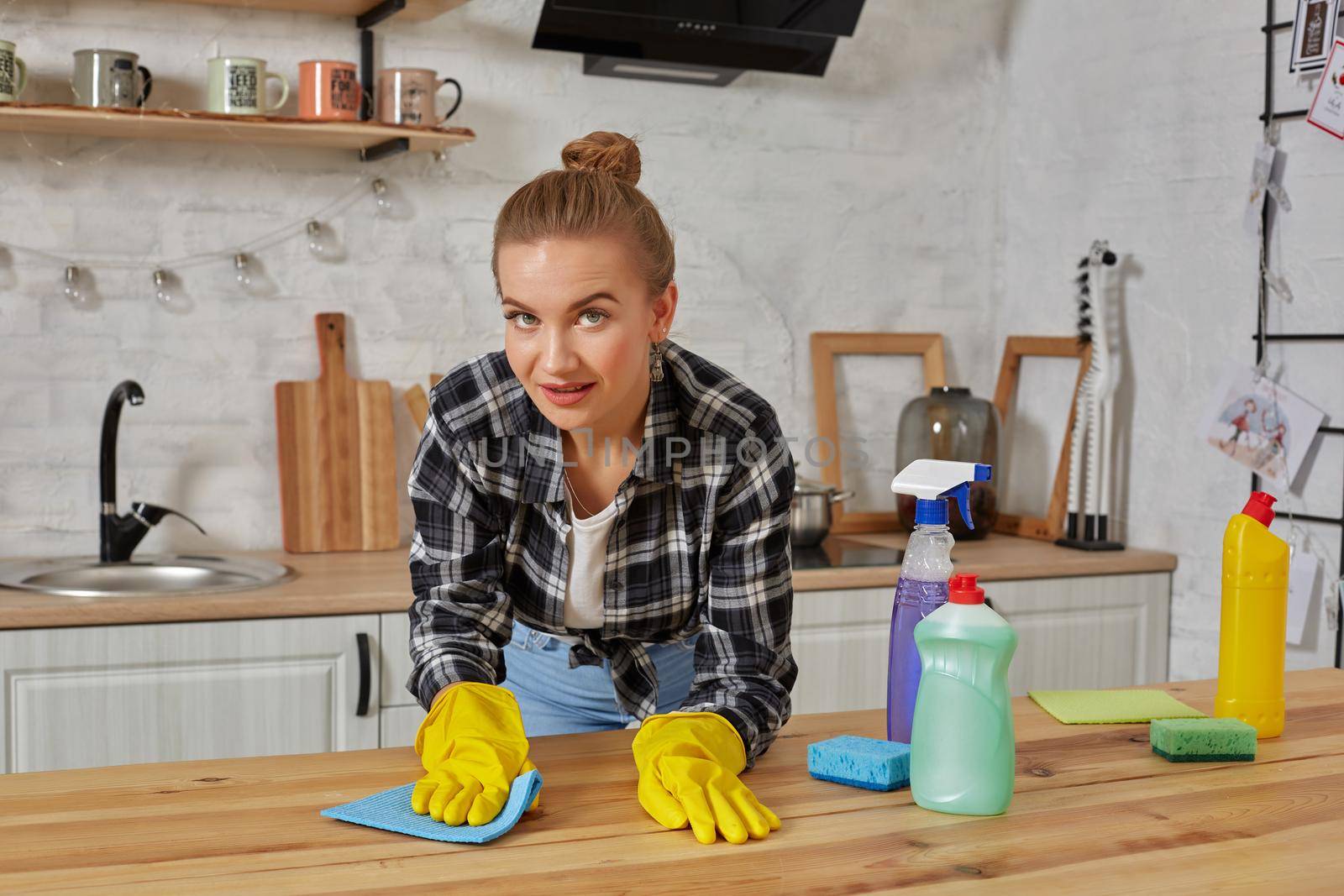 Household, cleaning and people concept - happy woman or housewife in rubber gloves wiping table with microfiber cloth at home kitchen.