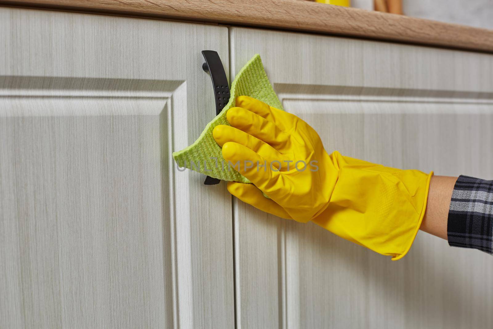 Hands in gloves with green rag is cleaning kitchen cabinets - housework and housekeeping concept. Close-up