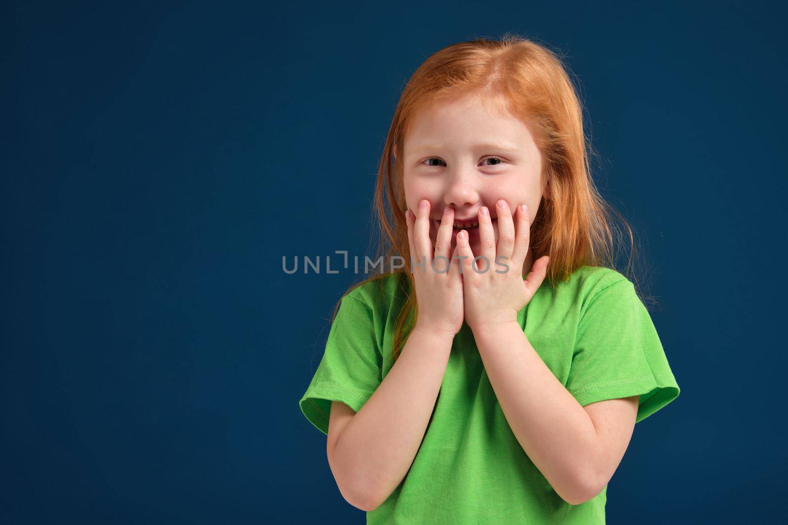 Cute little girl, in green t-shirt surprised by something, she feels emotional lift, blue background