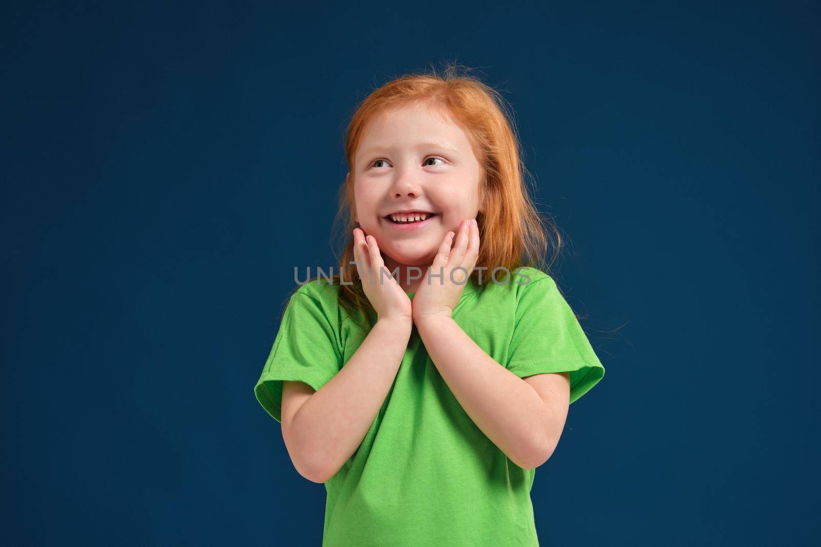Cute little girl, in green t-shirt surprised by something, she feels emotional lift, blue background
