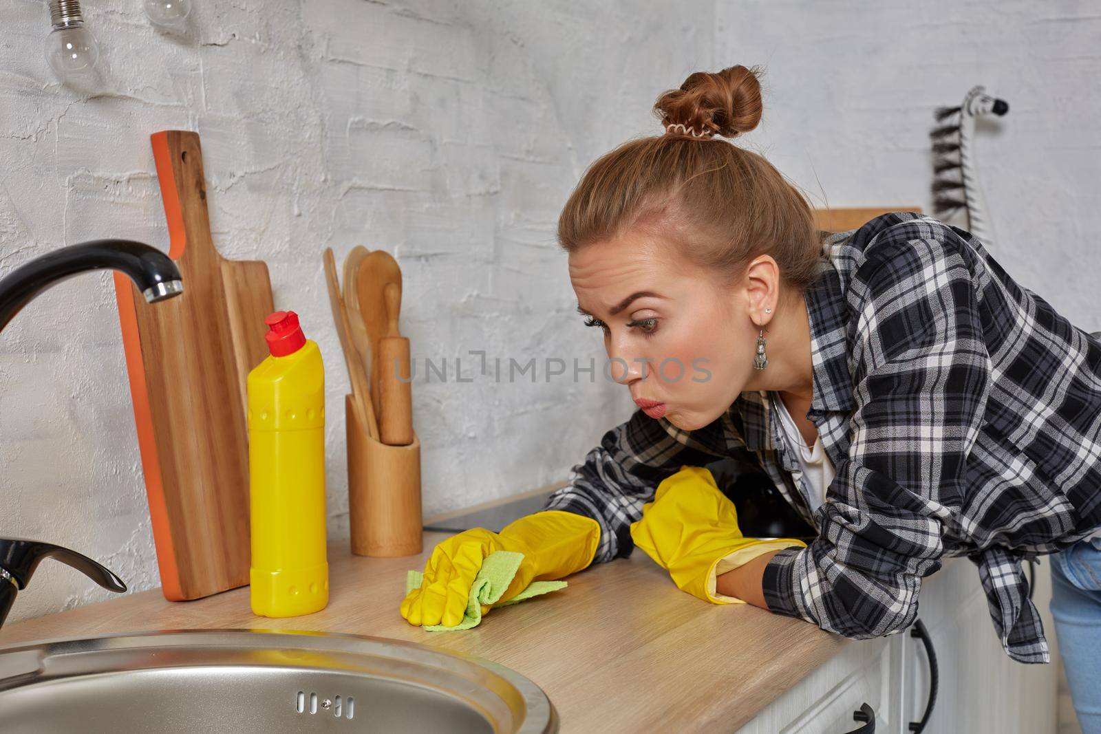 Hand cleaning. Young housewife woman washing sink in kitchen. Young woman washing manually, by hand, wearing yellow cleaning rubber gloves.