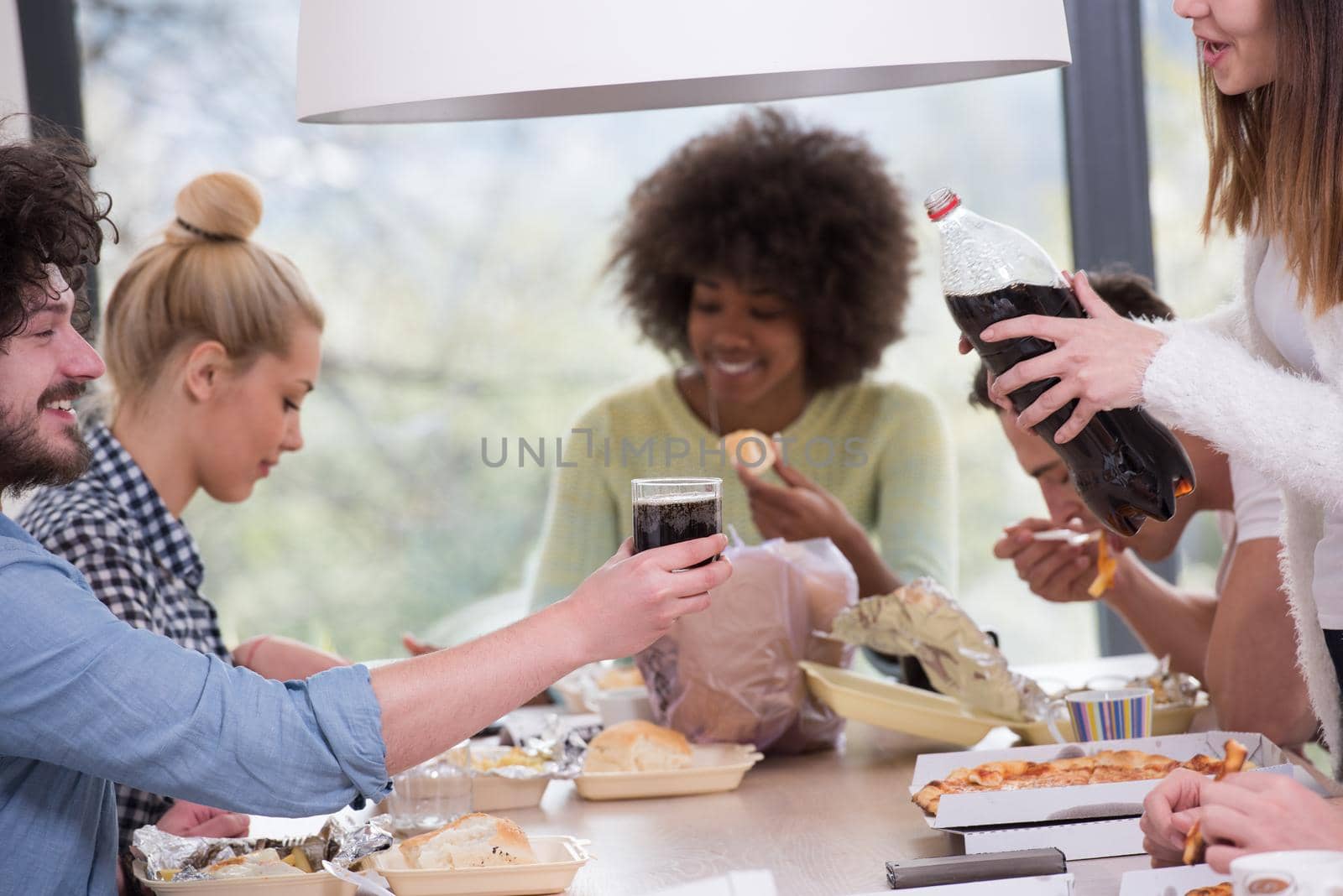 multiethnic group of happy friends spending time together with food and soda drinks, eating at home concept