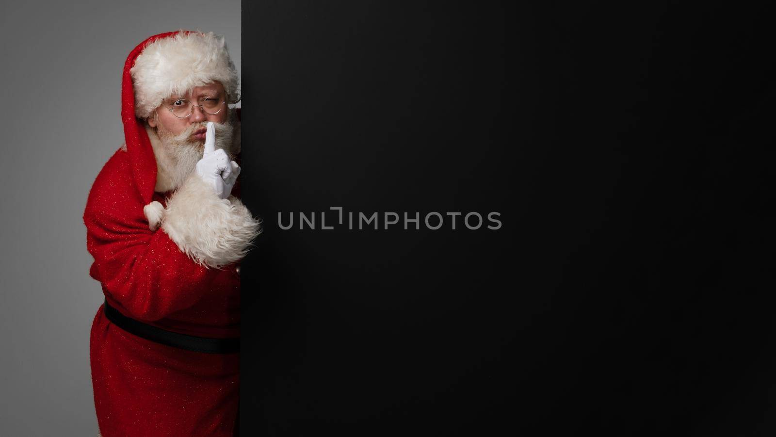 Santa Claus holding his finger on lips to have silence surprise concept, big black banner with copy space for text